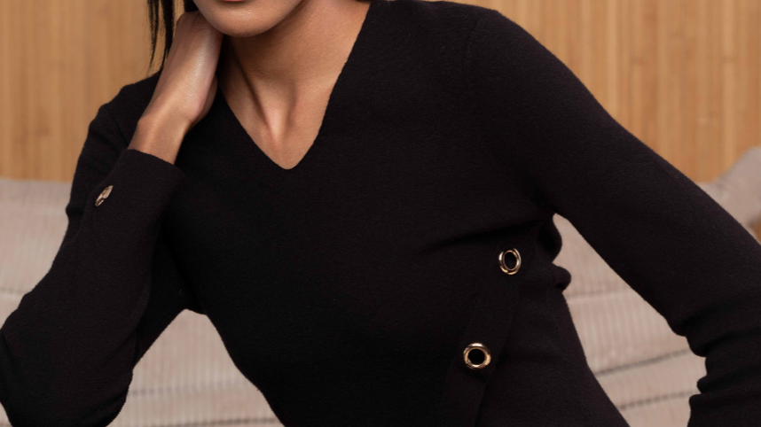 Woman wearing a black outfit with gold buttons against a wooden background
