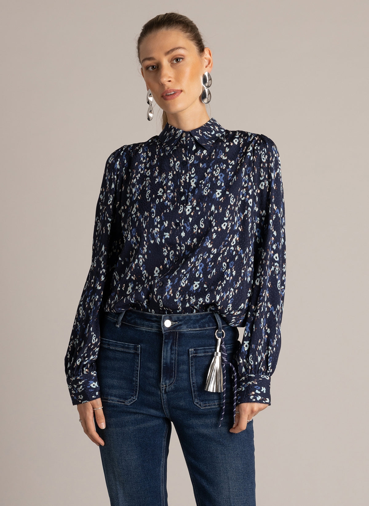 Woman wearing a navy printed button-front blouse with point collar, styled with dark wash jeans.