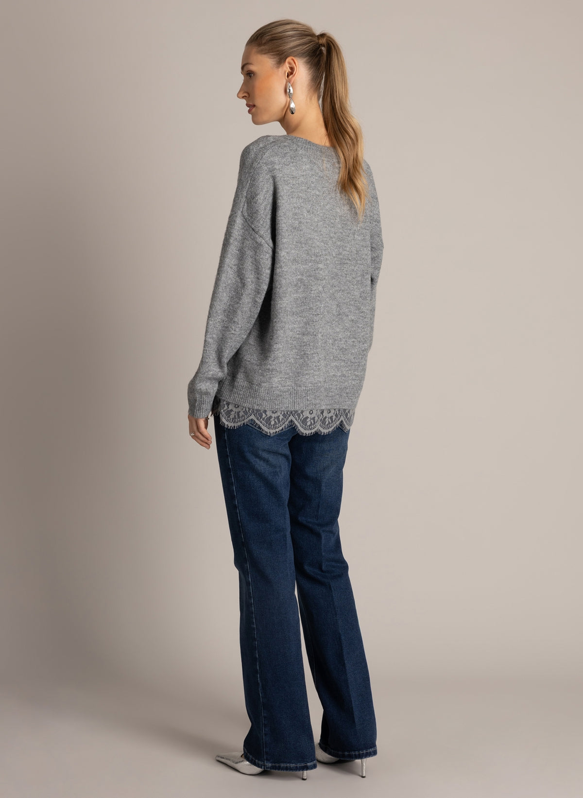 Back view of a grey sweater showing the relaxed silhouette and lace trim peeking out along the hem, paired with denim.