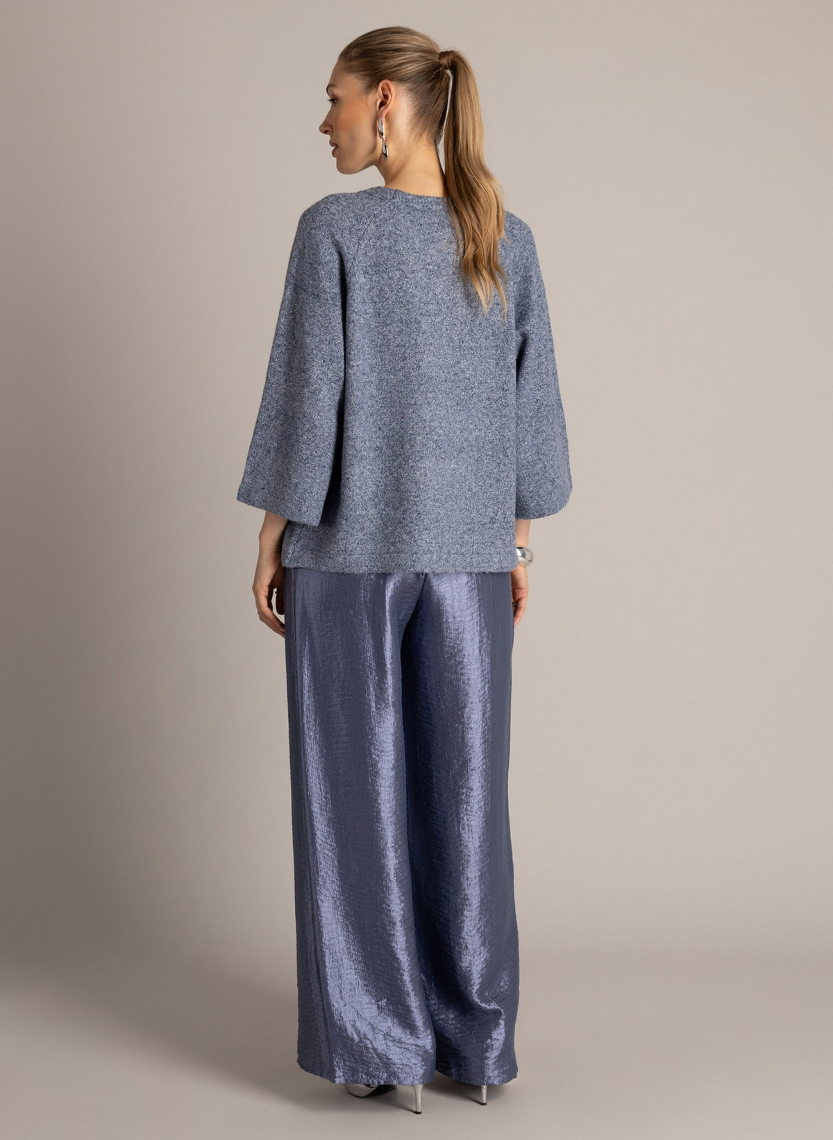 Model wearing a blue-grey textured knit top with three-quarter sleeves and wide-leg, metallic blue-grey trousers.
