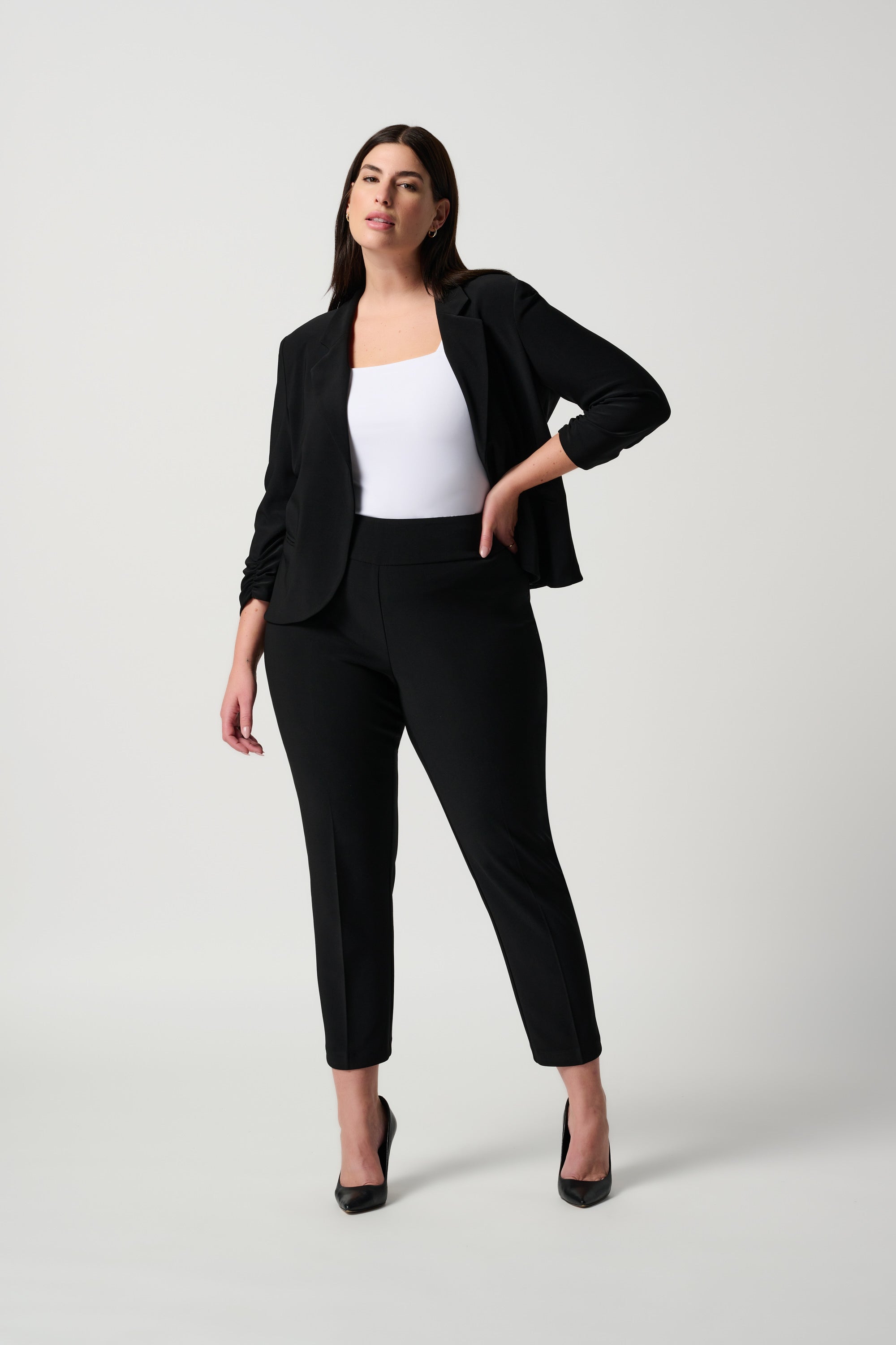 Plus sized woman wearing a black suit with a white top on a light gray background