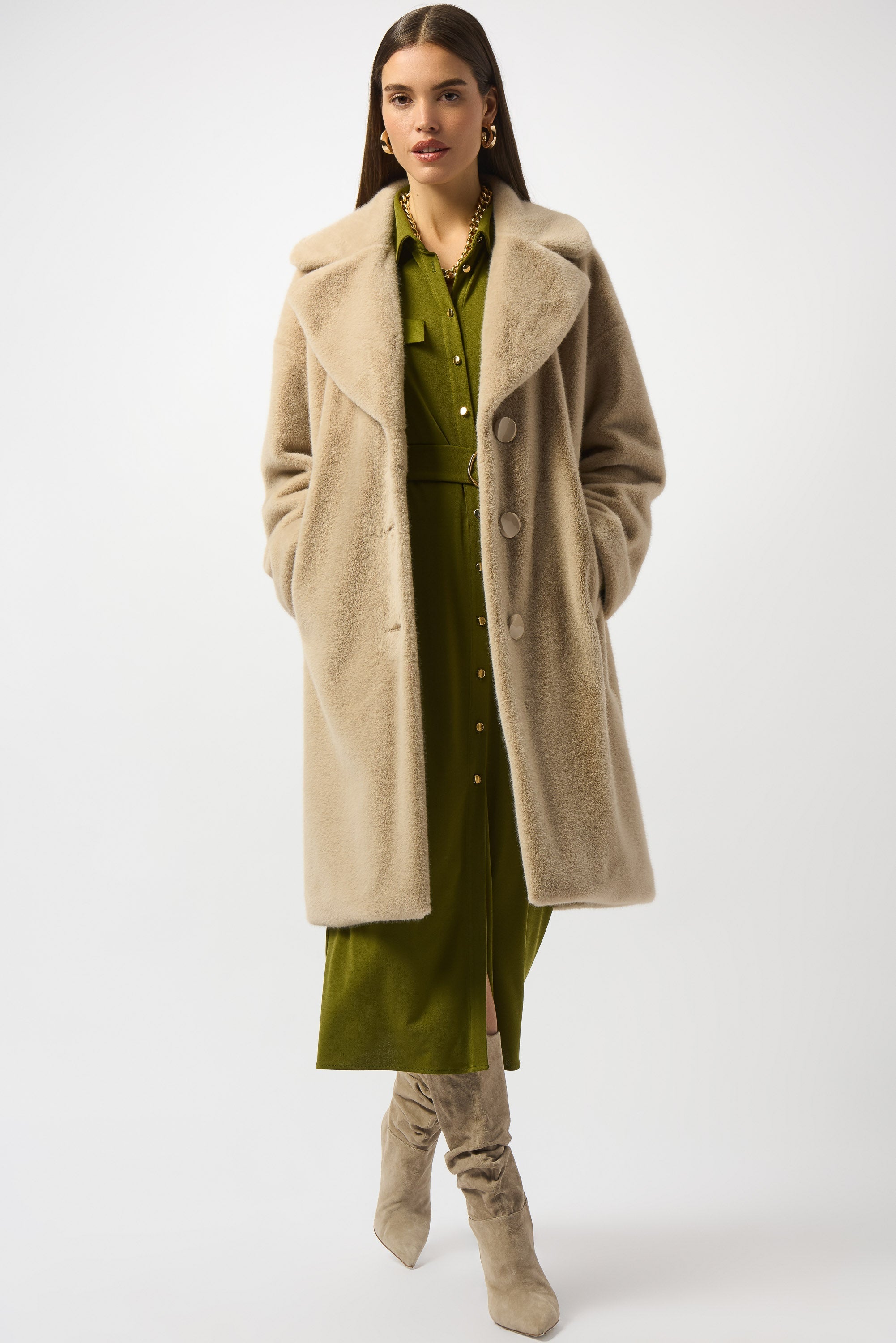 Woman wearing a beige coat over a green dress with beige knee-high boots on a white background