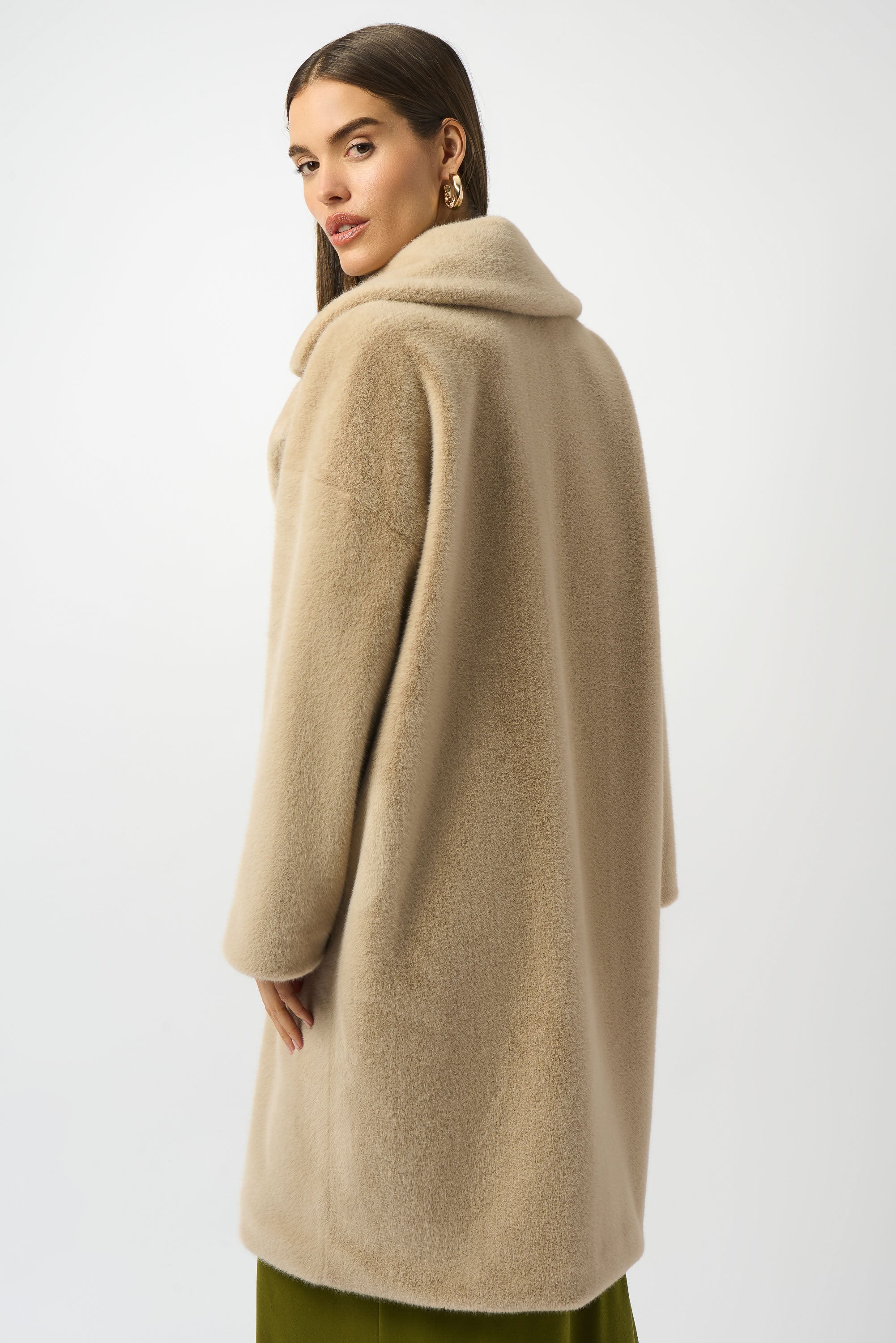 Woman wearing a beige coat on a white background facing backwards