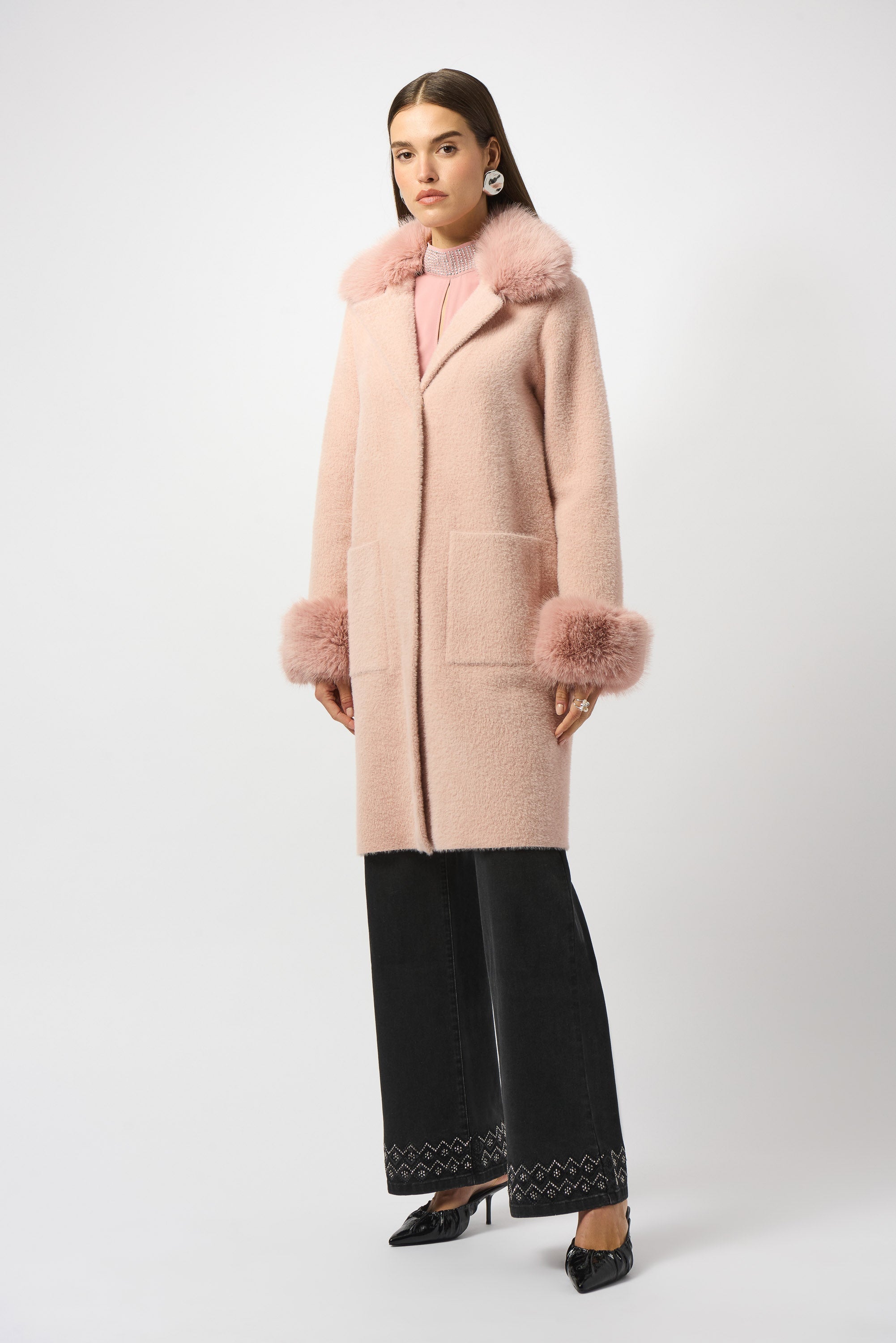 Woman wearing a long pink coat with fur trim on a white background