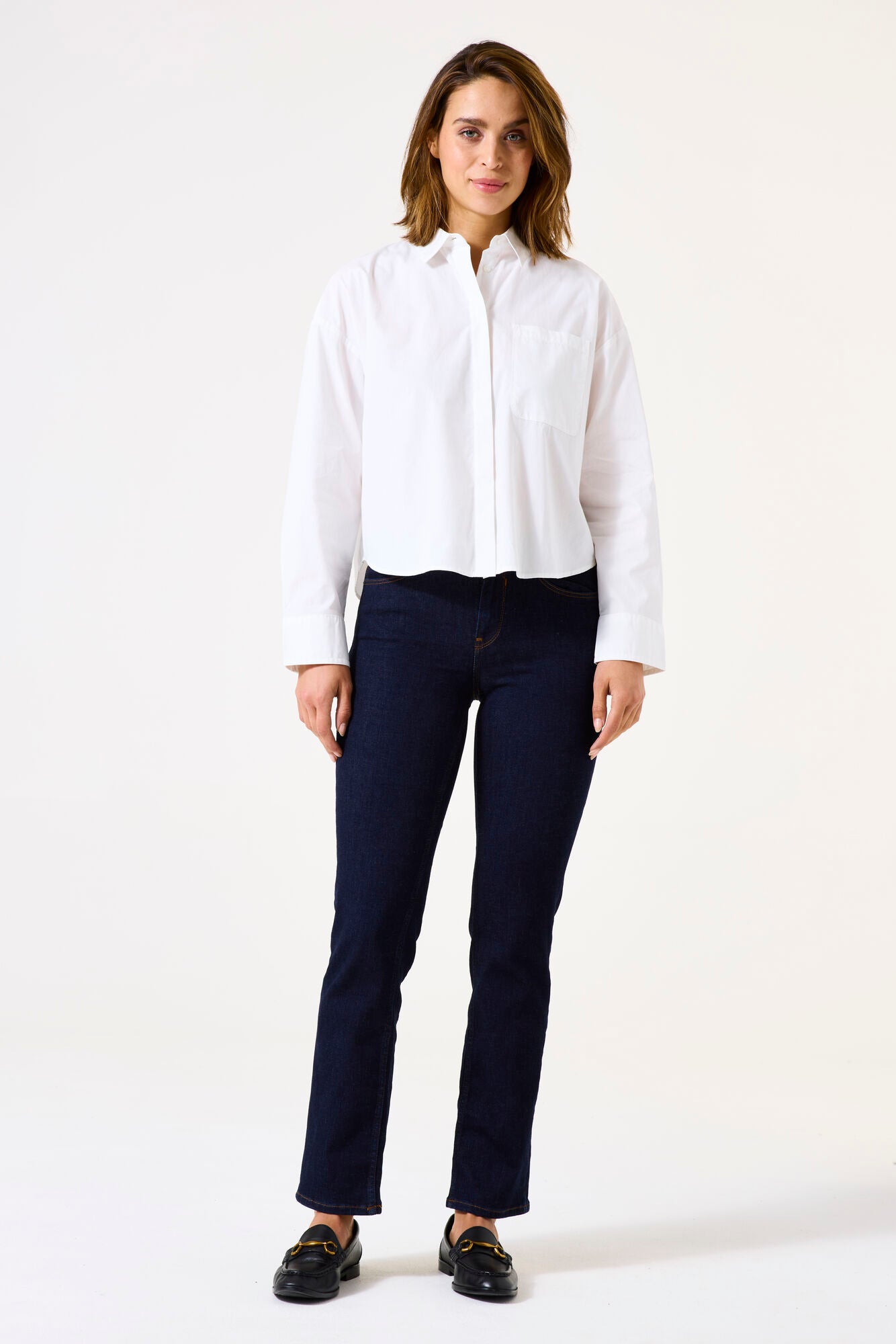 Woman wearing mid-rise straight-leg denim jeans with a fitted hip and clean five-pocket styling, front view.