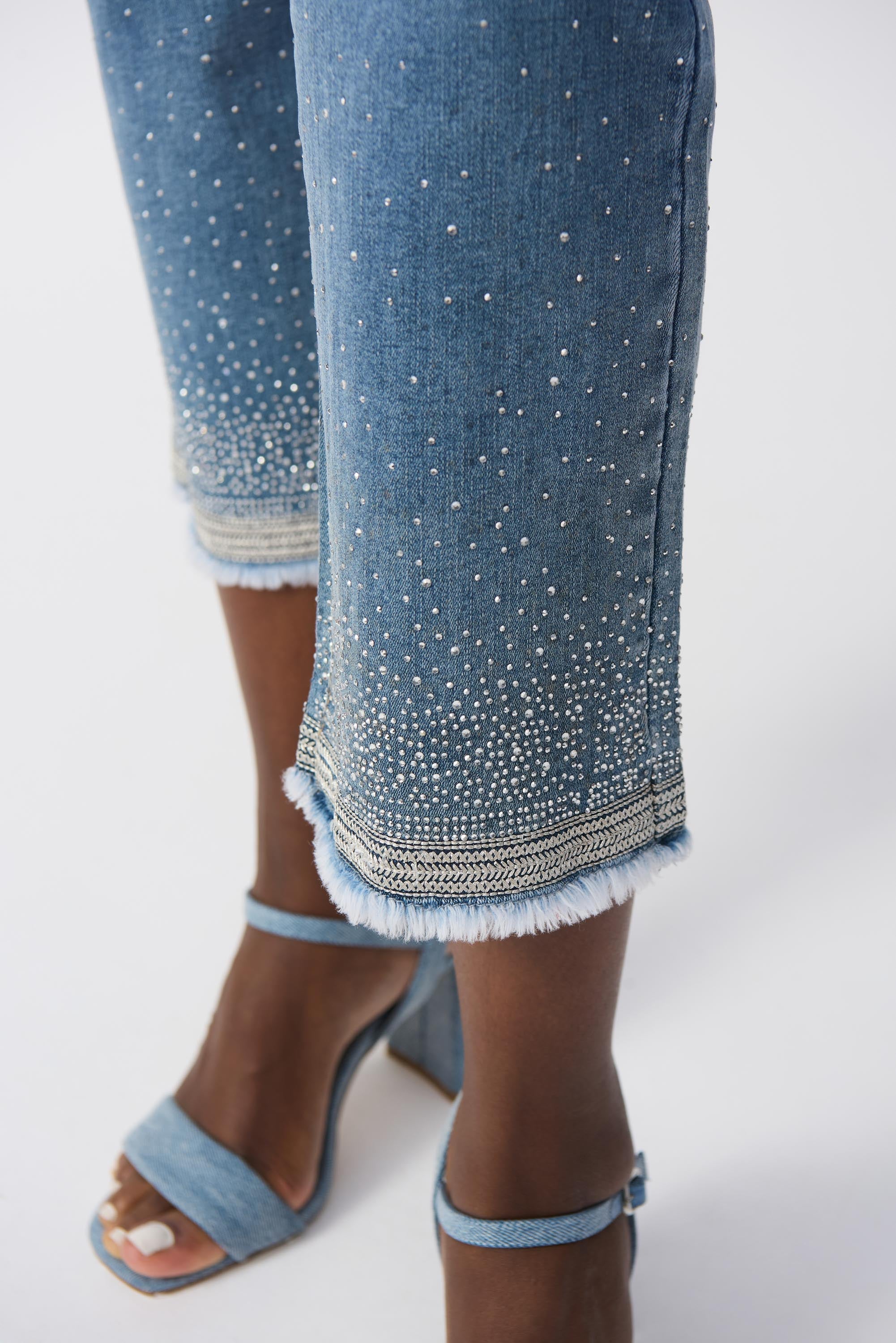 Zoomed-in view of hem showing embroidered trim and sparkling crystal detailing on cropped jeans.