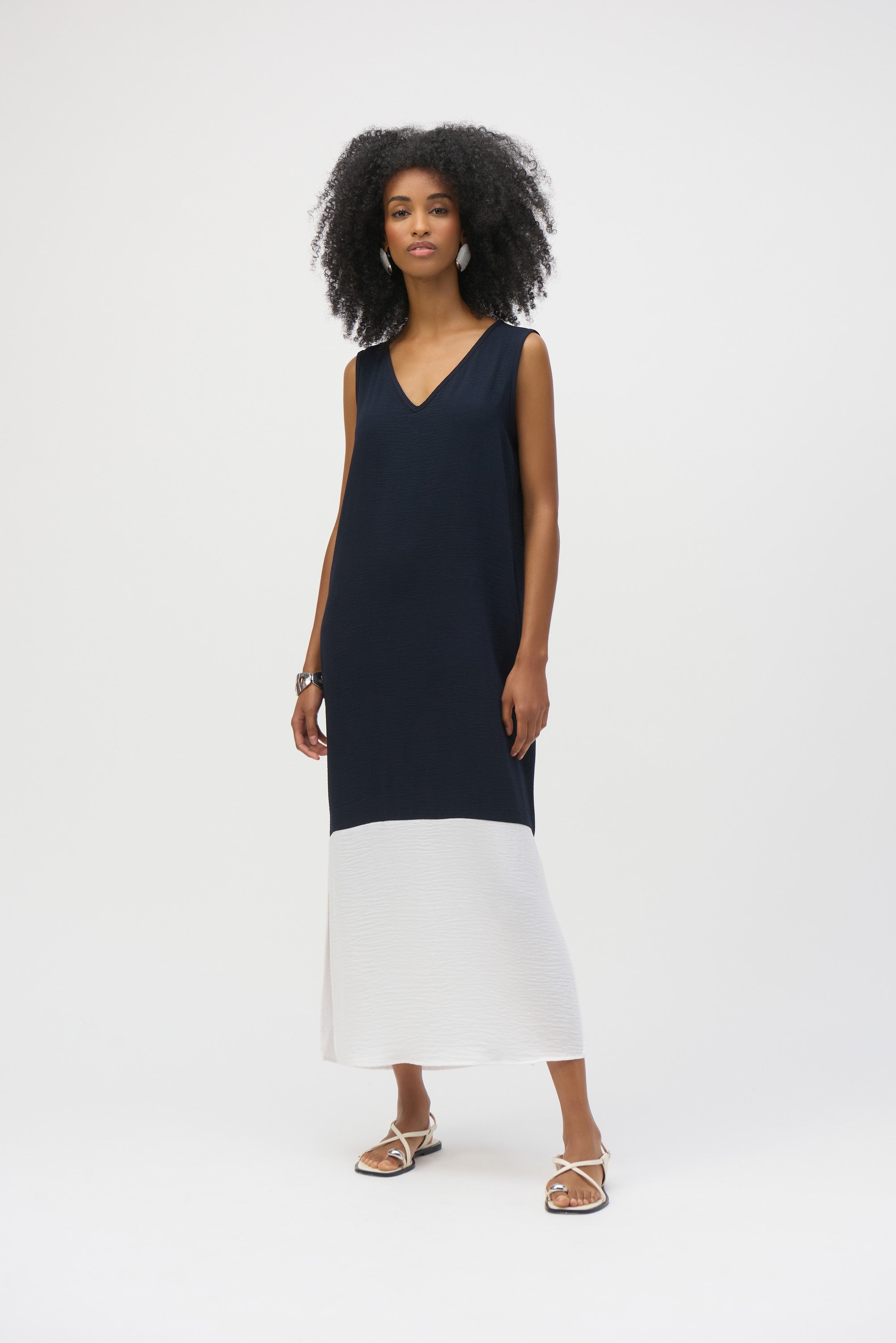 Model in a sleeveless navy and white midi dress with side slit details paired with flat sandals.