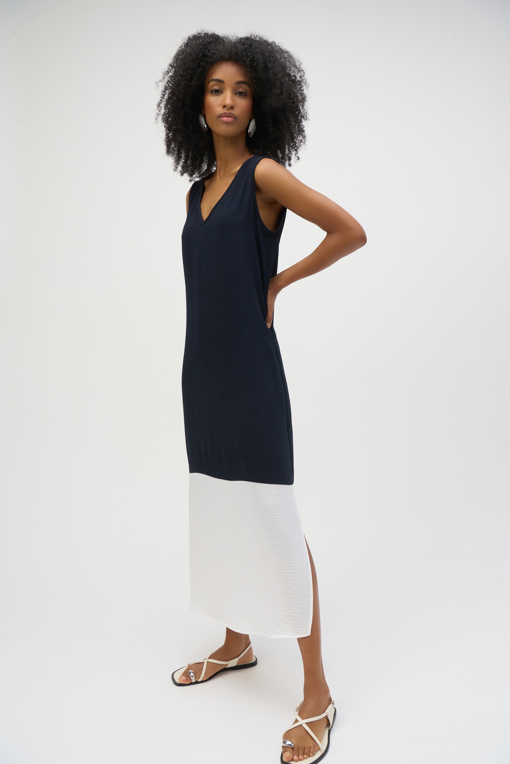 Model in a sleeveless navy and white midi dress with side slit details and a clean, minimalistic design, paired with flat sandals.