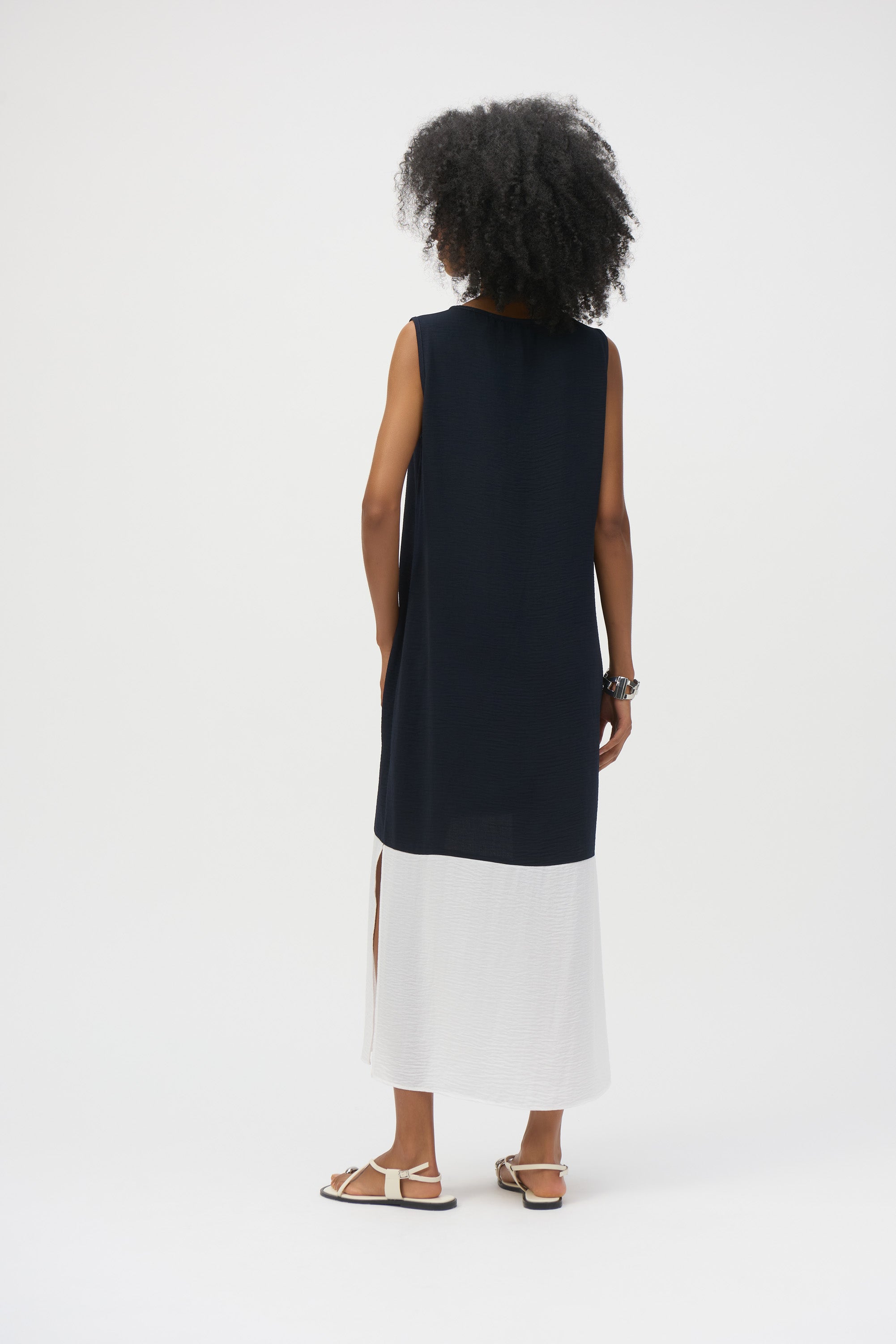 Back view of a model wearing the colourblock sleeveless dress with a navy top half and white bottom, showcasing side slits and a relaxed fit.