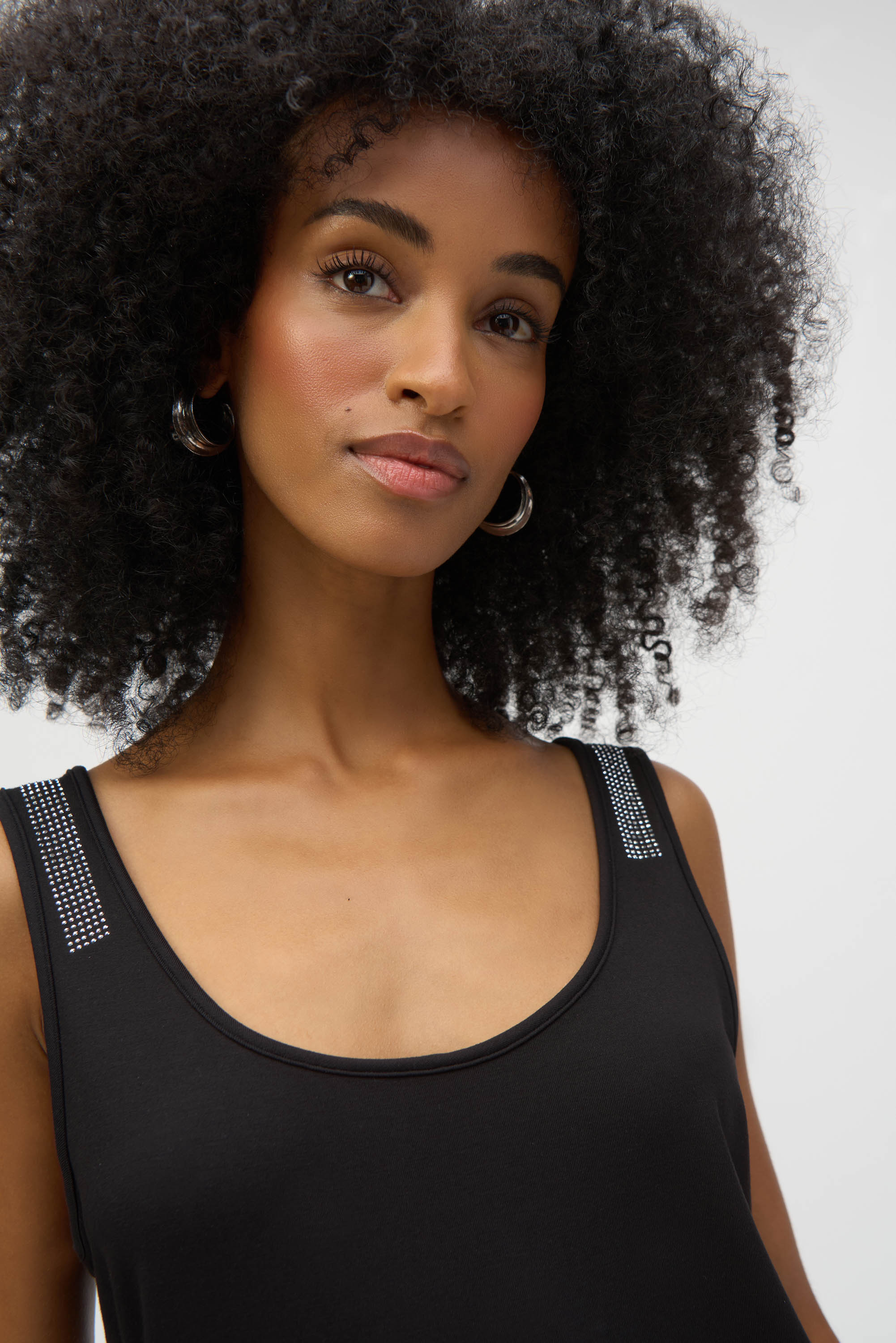 Close-up of woman wearing black tank top, showing rhinestone details on shoulder straps.