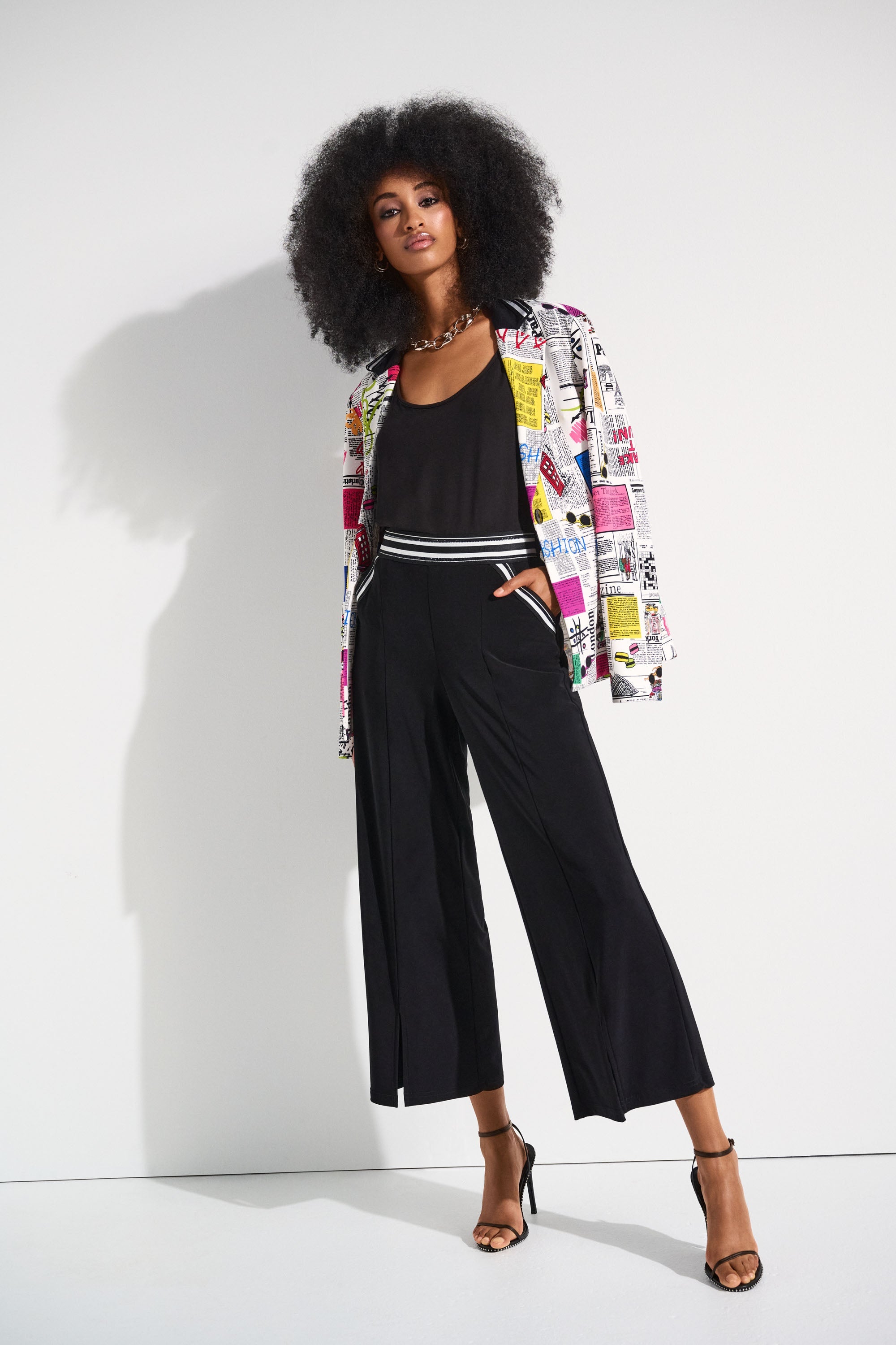 Woman wearing black tank top under a colourful graphic blazer with high-waisted black culottes and heels.