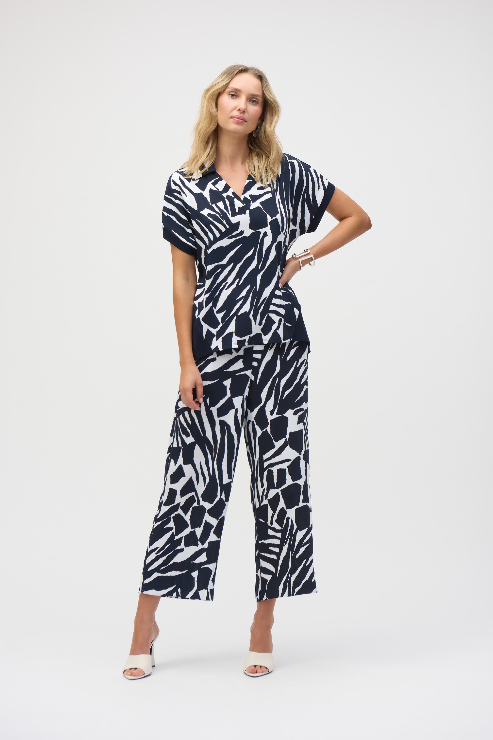 Woman in full-length view wearing the abstract print blouse with matching wide-leg pants and white heeled sandals.