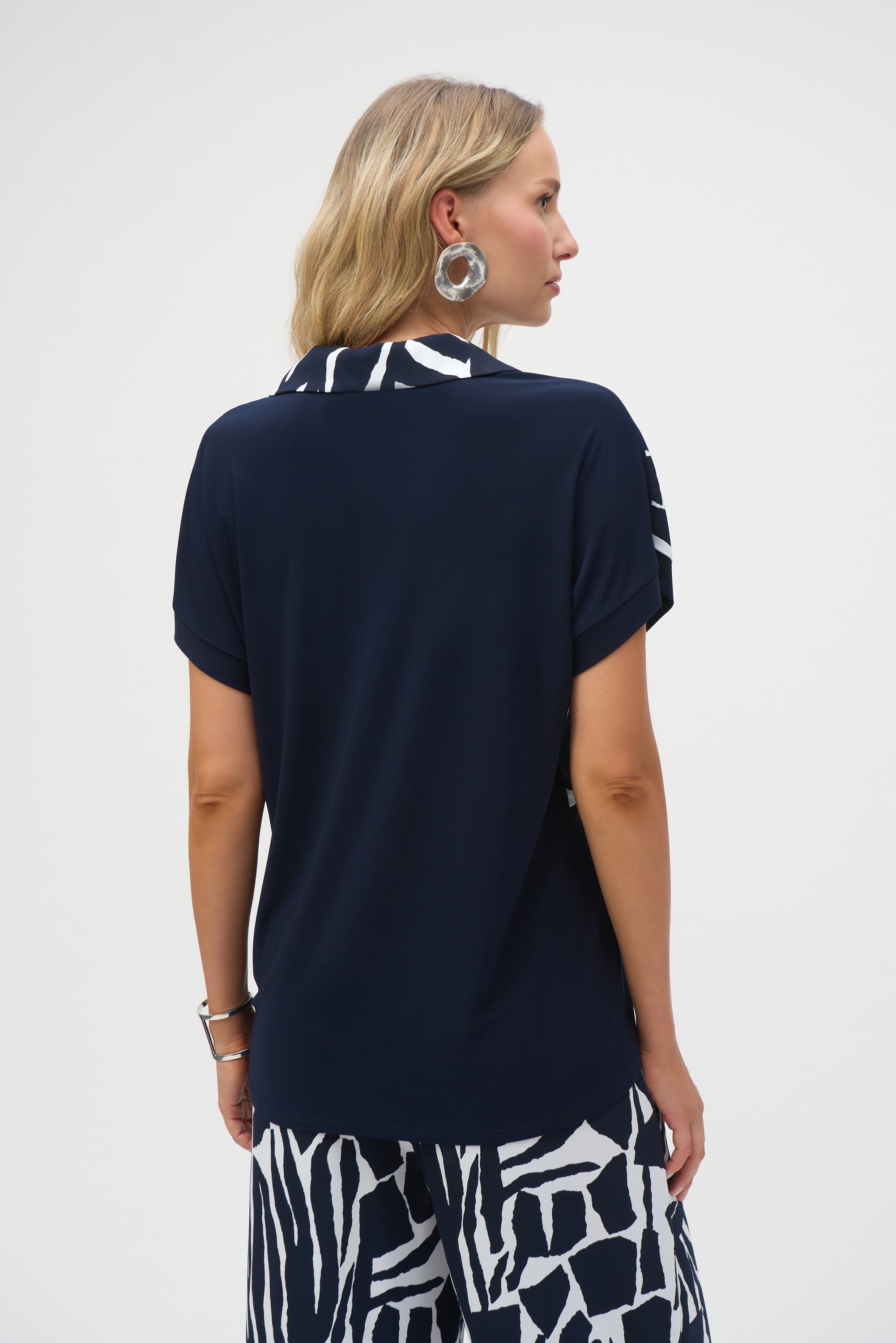 Back view of a woman wearing the solid navy back of the short sleeve blouse paired with matching abstract print pants.