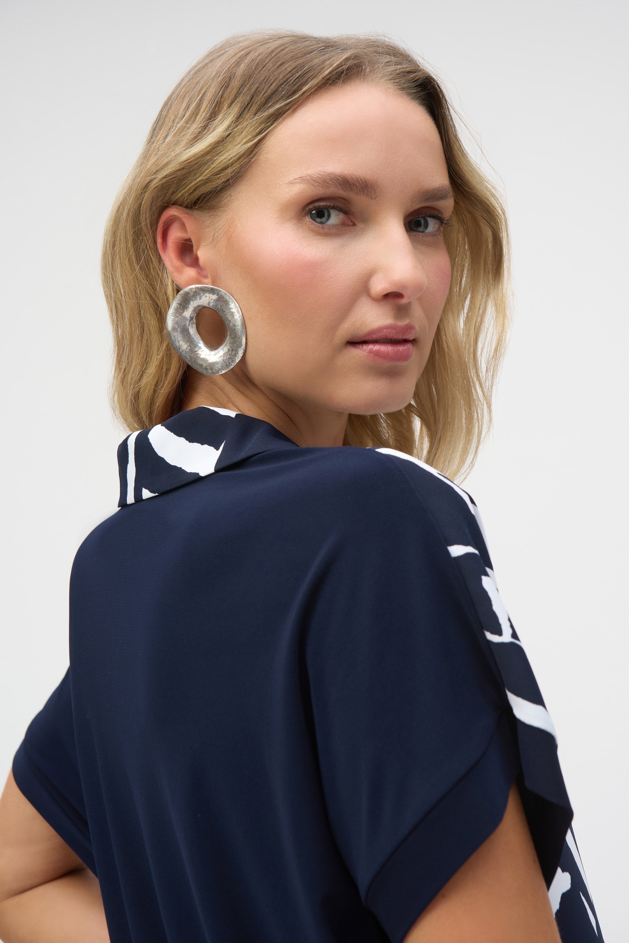 Close-up side view of a woman wearing the abstract print blouse, highlighting a large silver statement earring.