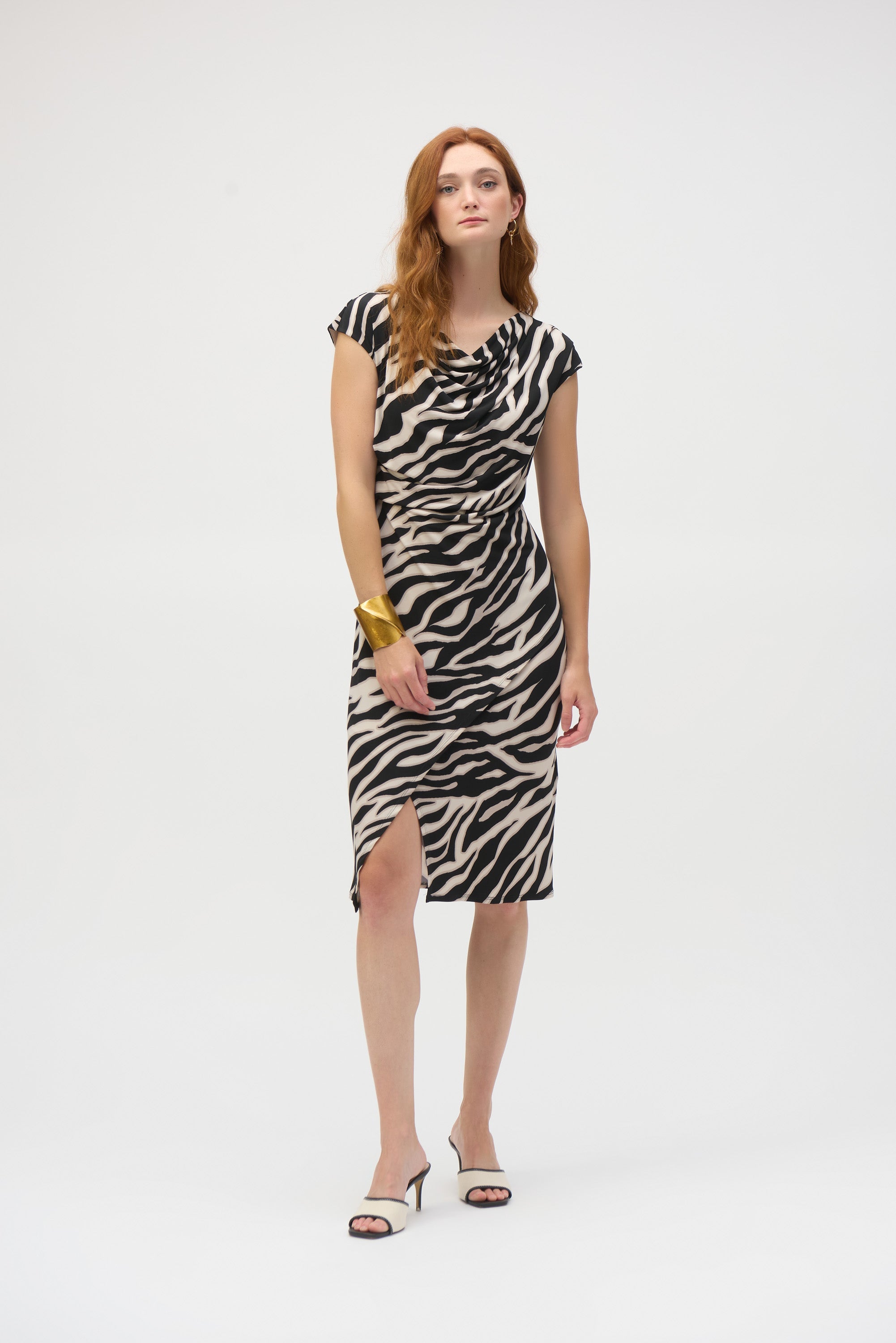 Full body front view of woman wearing zebra print dress with side slit and gold cuff bracelet.