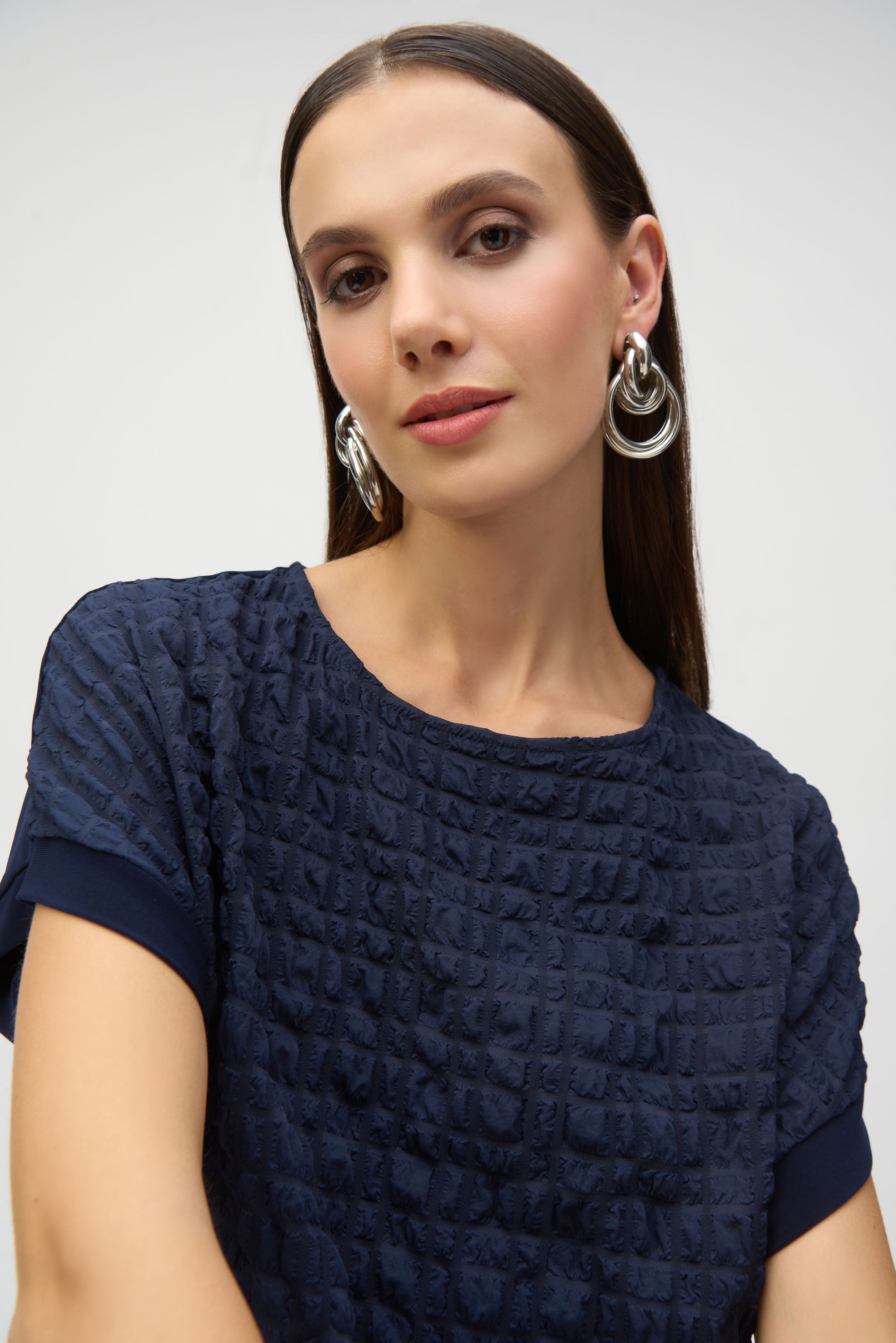 Close-up of woman wearing a navy textured top with short sleeves, showcasing the fabric detail and silver hoop earrings.