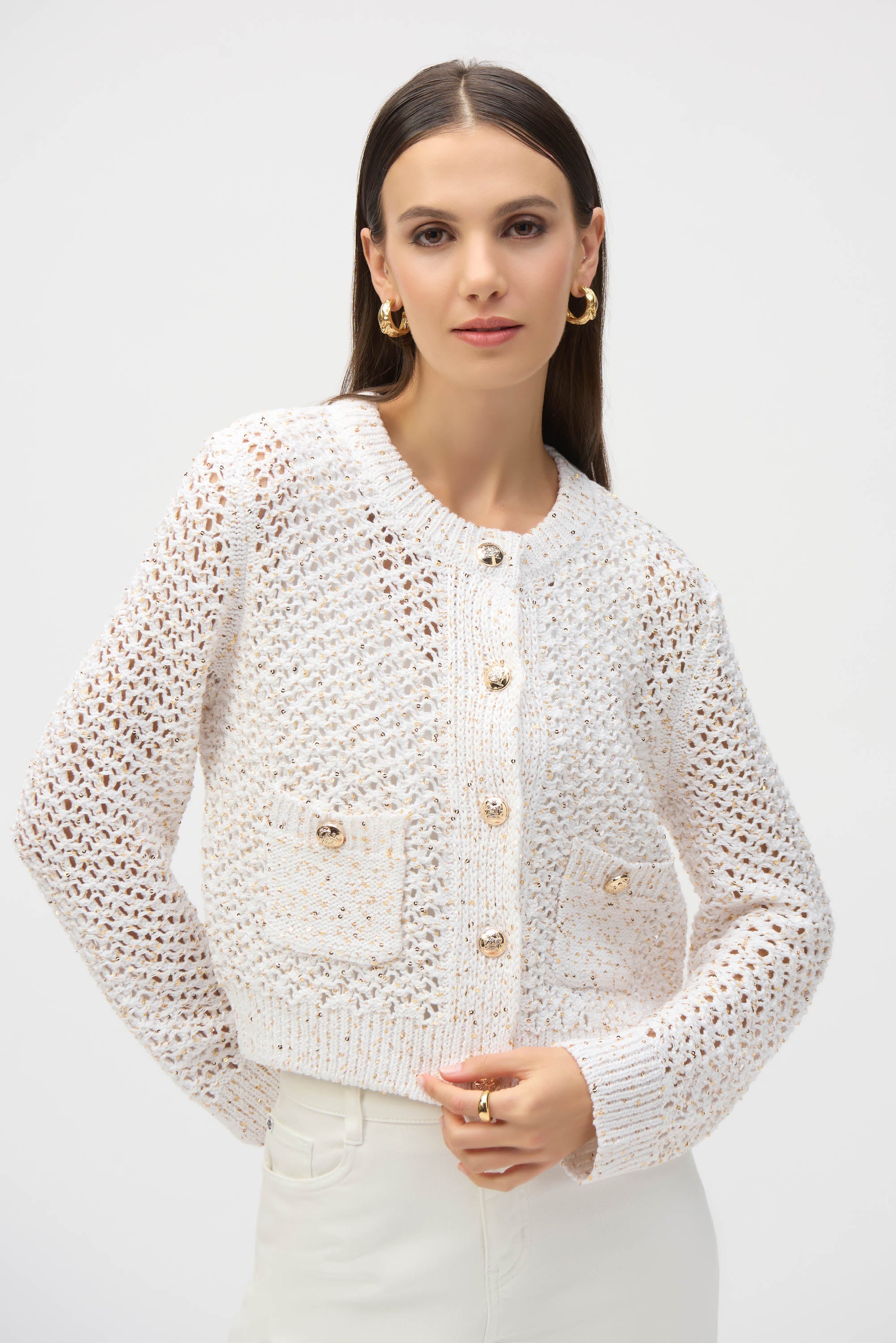 Mid-shot of woman wearing cream open knit cardigan with gold-tone buttons and patch pocket details.