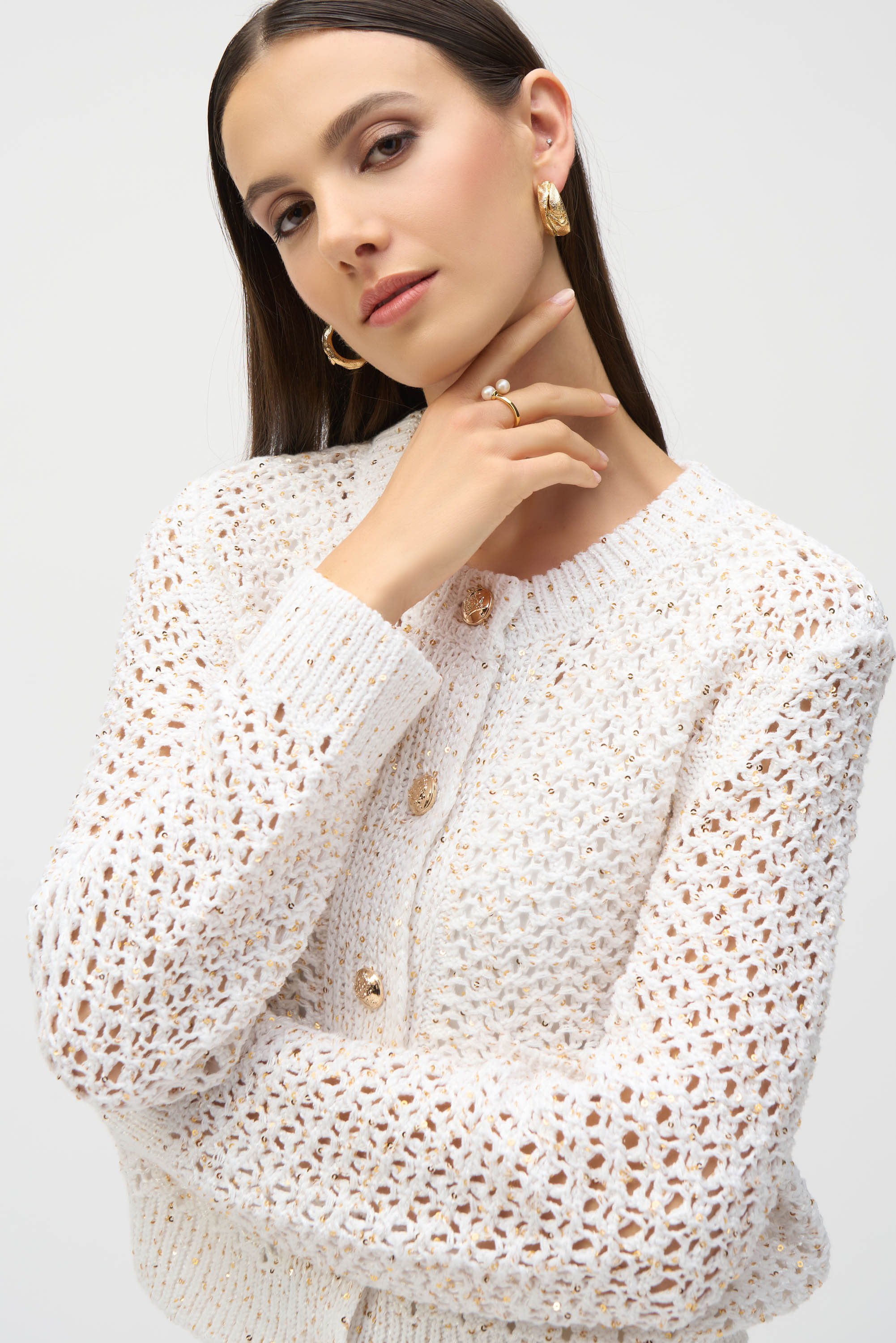 Close-up of woman wearing gold jewellery and textured cream cardigan with open knit pattern.