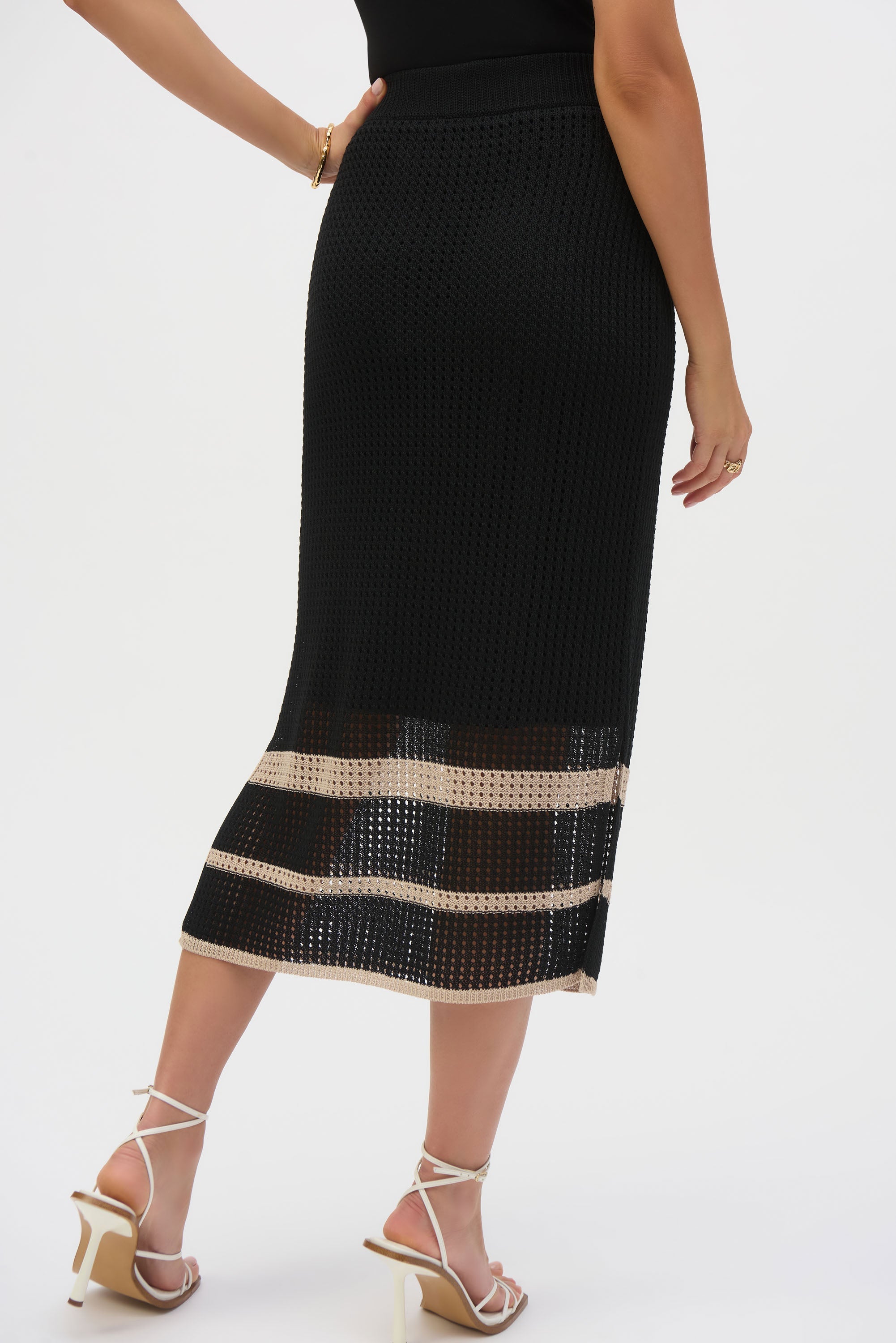 Woman wearing black open-stitch midi skirt with beige stripes and side slit, styled with strappy heels.