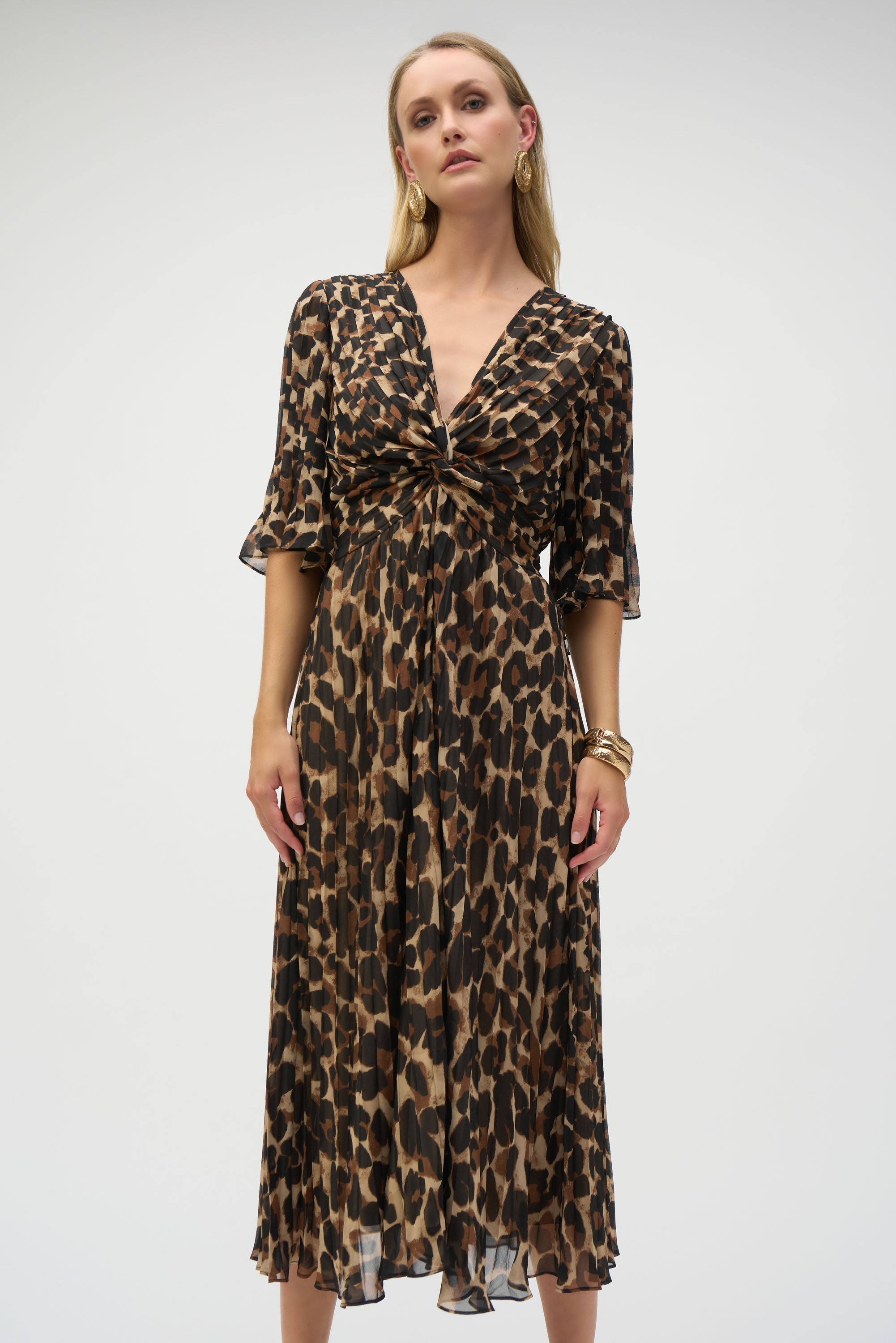 Woman wearing V-neck animal print chiffon midi dress with twist detail and pleated skirt, styled with gold earrings and bangles.