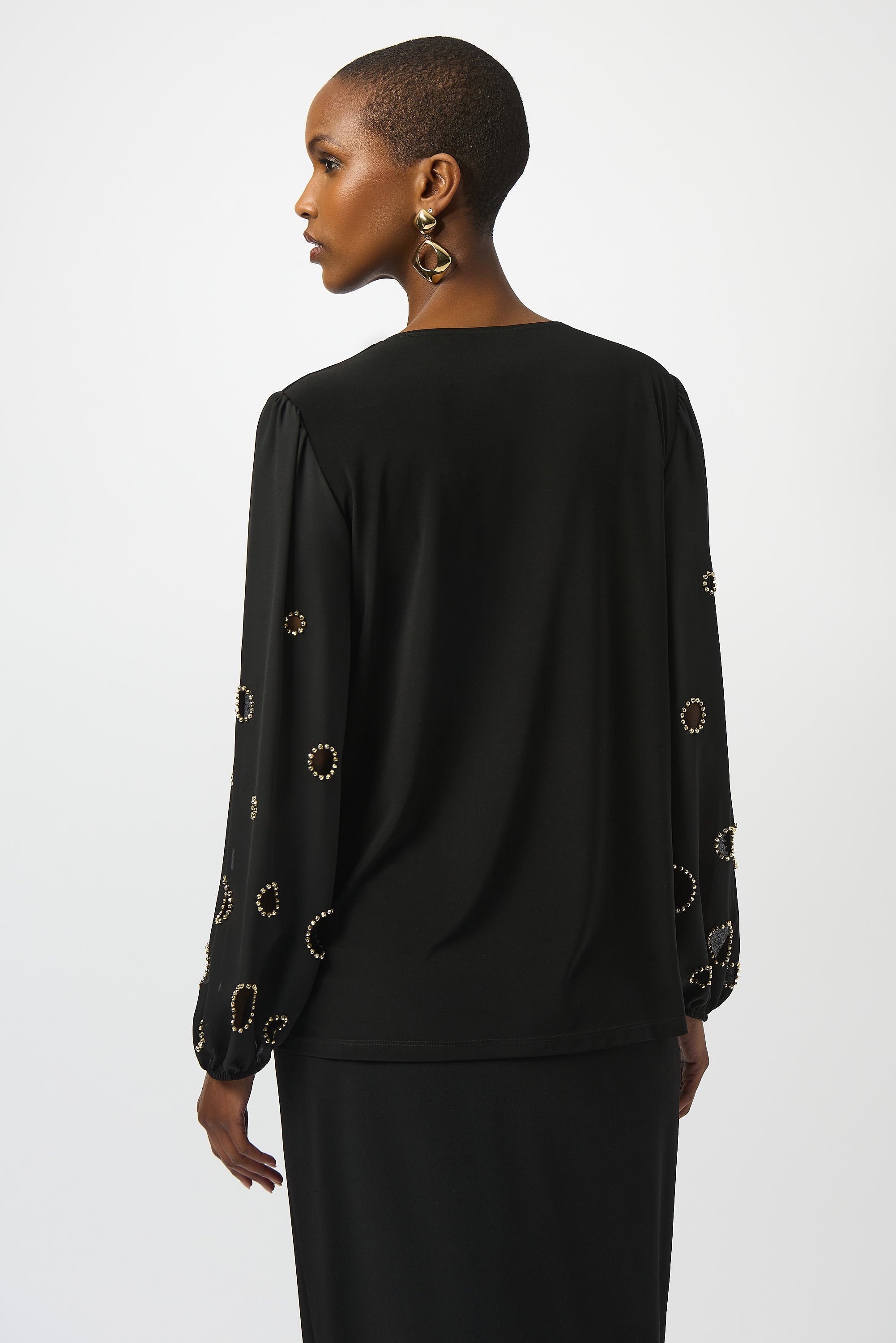 woman standing with her back towards us in a black top with a beaded pattern on the sleeves