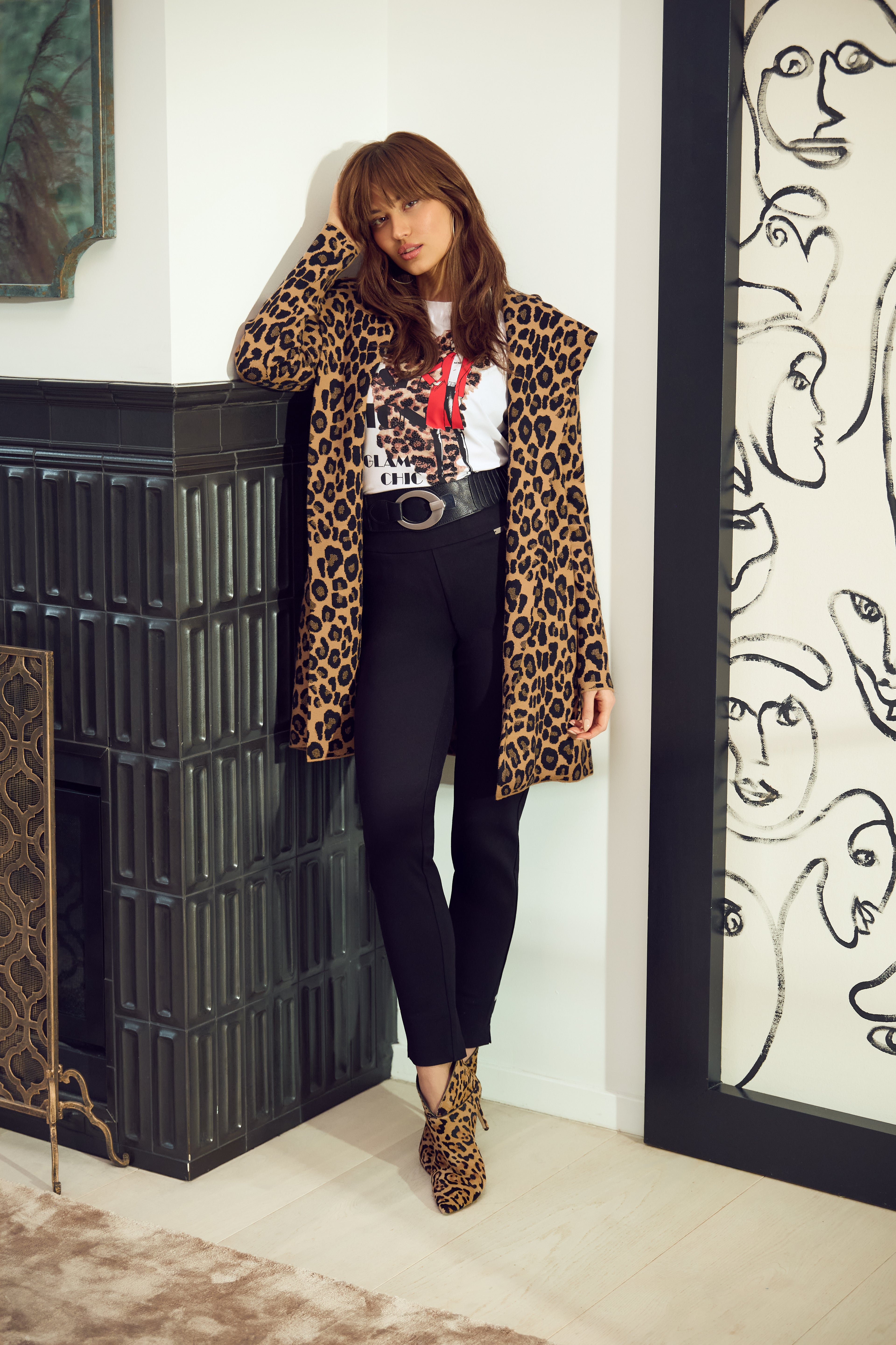 Person wearing a leopard print coat in an interior setting with a fireplace and decorative wall.