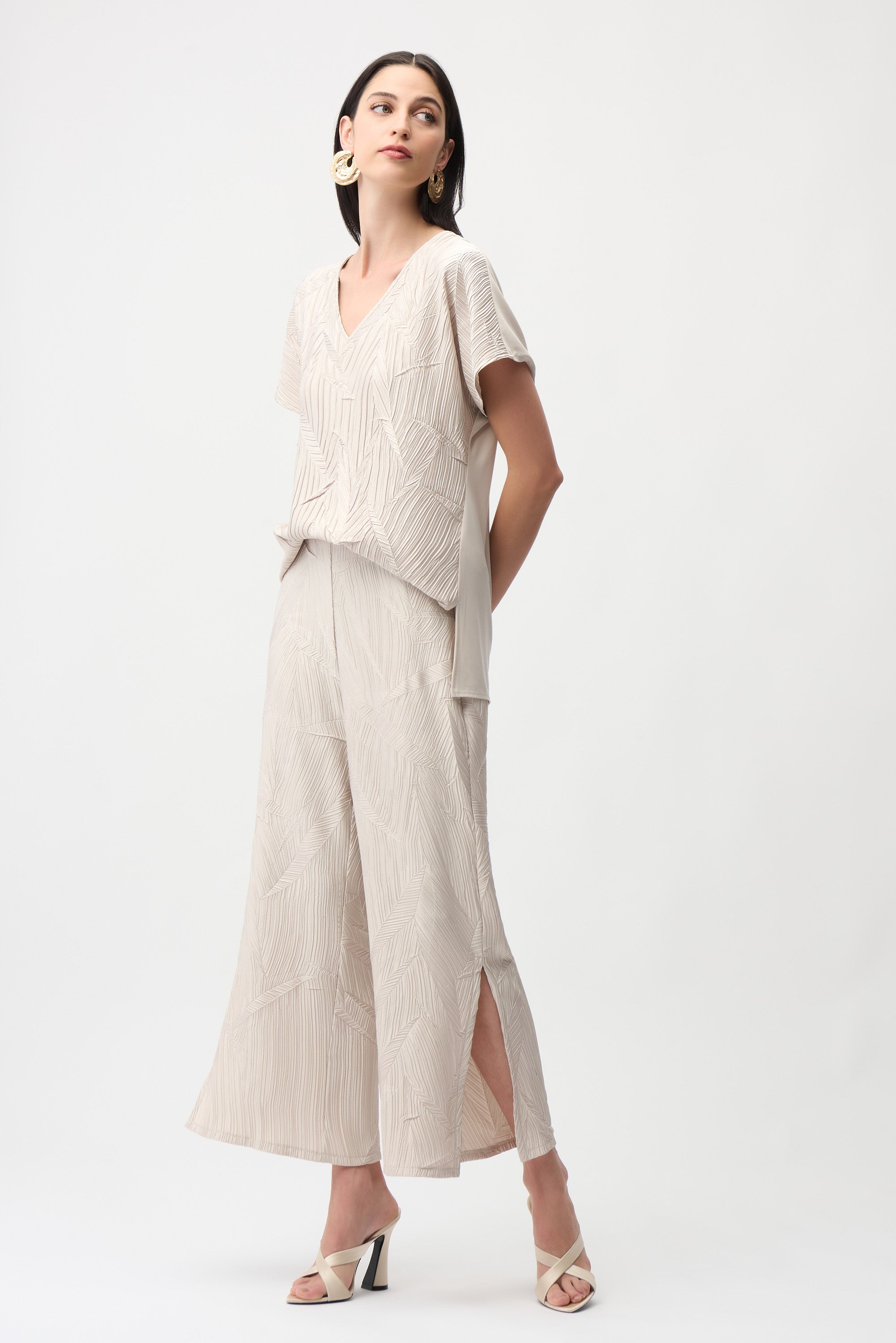 Model wearing pleated satin pull-on culotte pants with side slits, showcasing luxurious geometric texturing and a polished look.