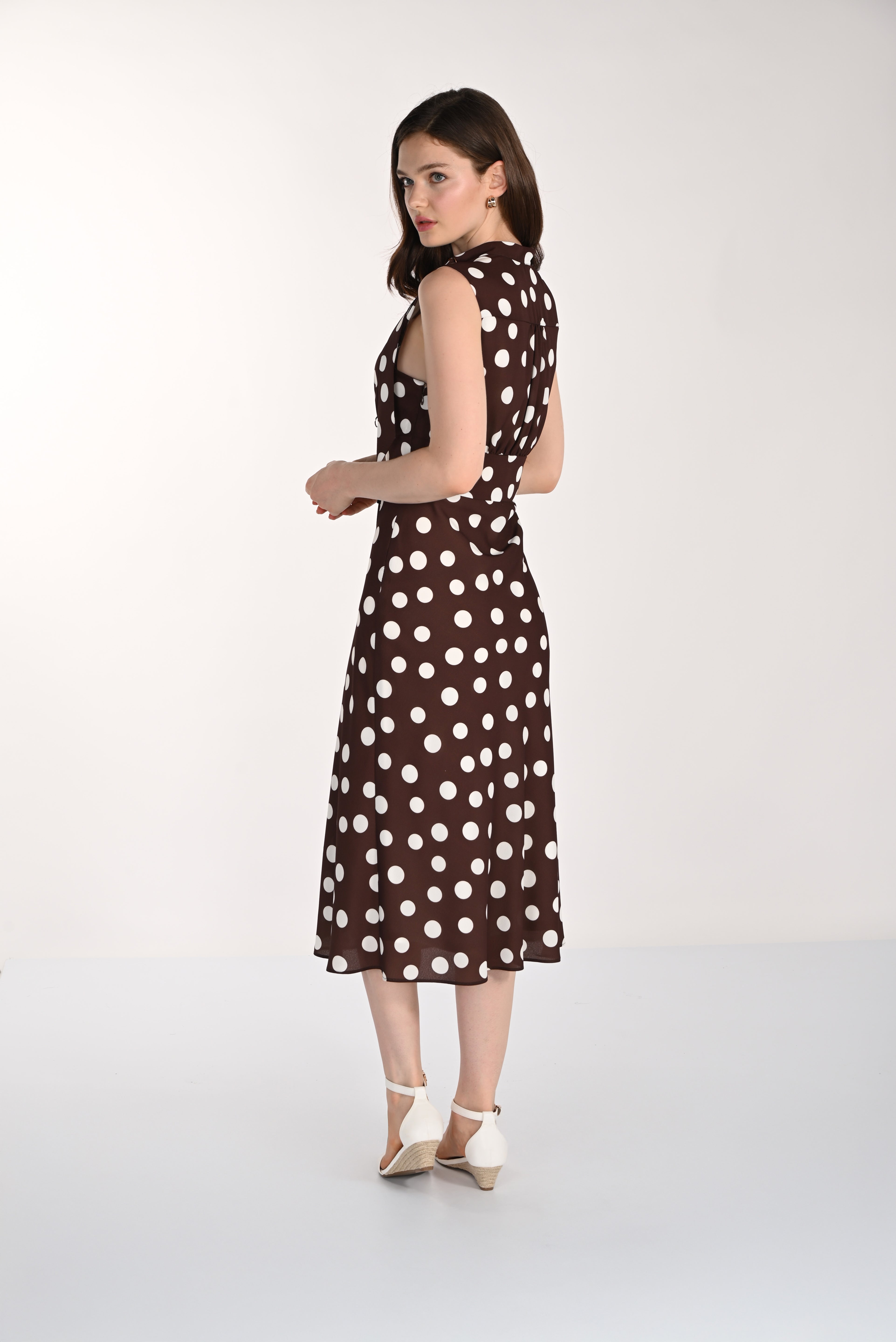 Women's sleeveless polka dot midi dress with a tie-neck detail, fitted waist, and flowing skirt. Shown from the back and side to highlight the silhouette and drape.