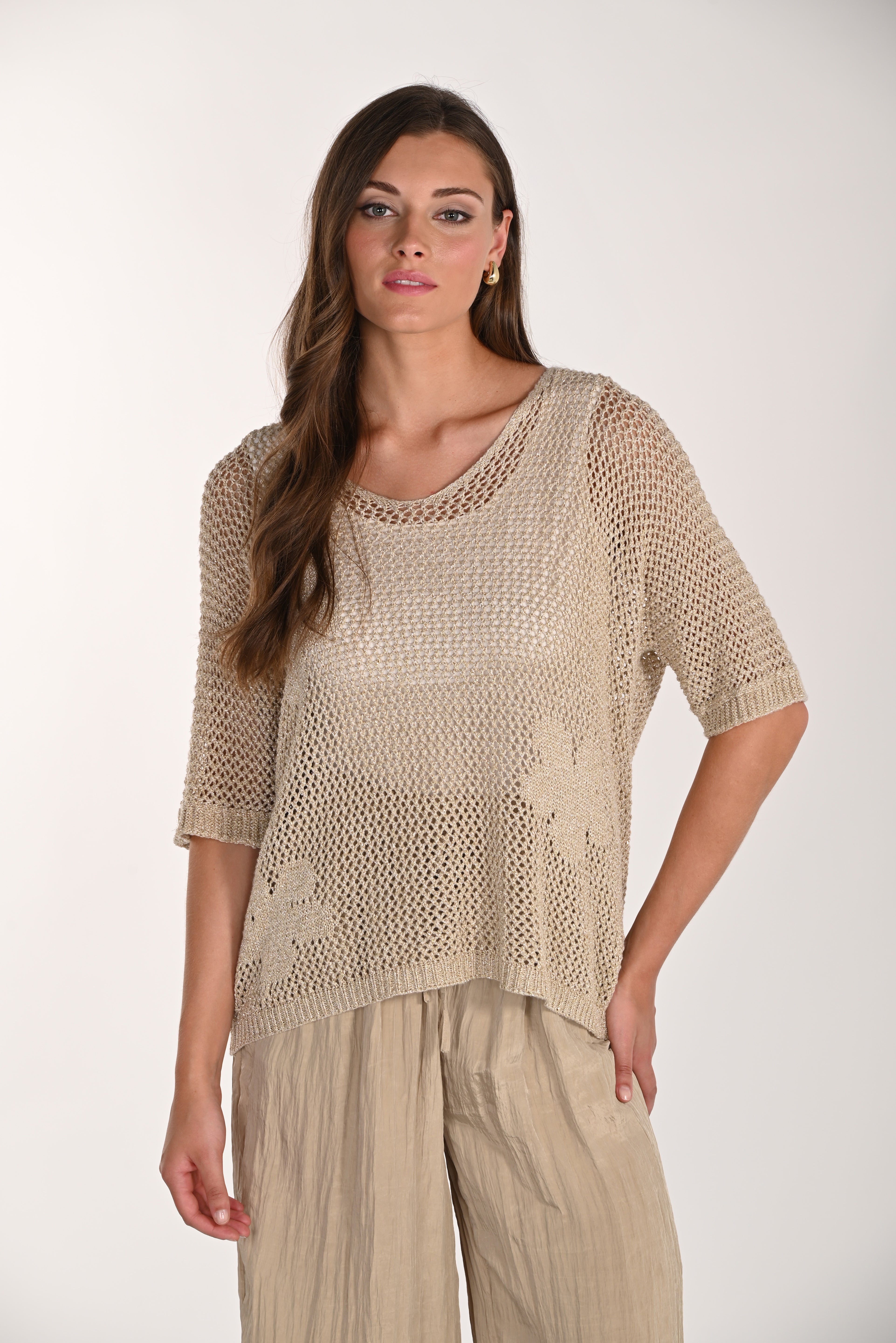 Woman modelling a beige metallic open-knit top with a relaxed fit, round neckline, and elbow-length sleeves. The lightweight mesh-knit texture features a subtle shimmer and is paired with loose, crinkled wide-leg trousers.
