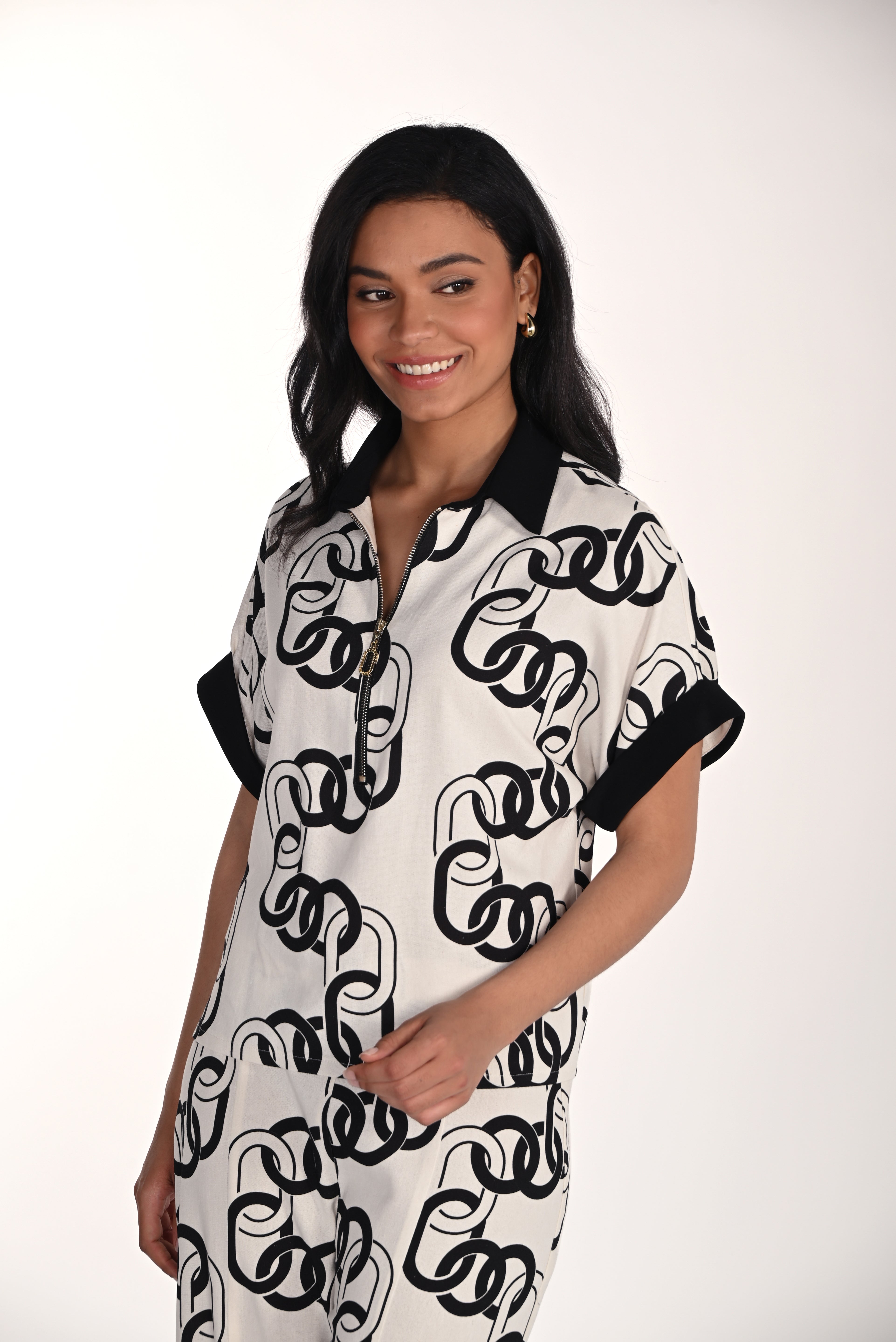 Woman wearing a relaxed-fit chain print blouse with a collared zip neckline and cuffed short sleeves, styled with matching wide-leg pants. Front angled view showcasing the lightweight drape and modern printed design.