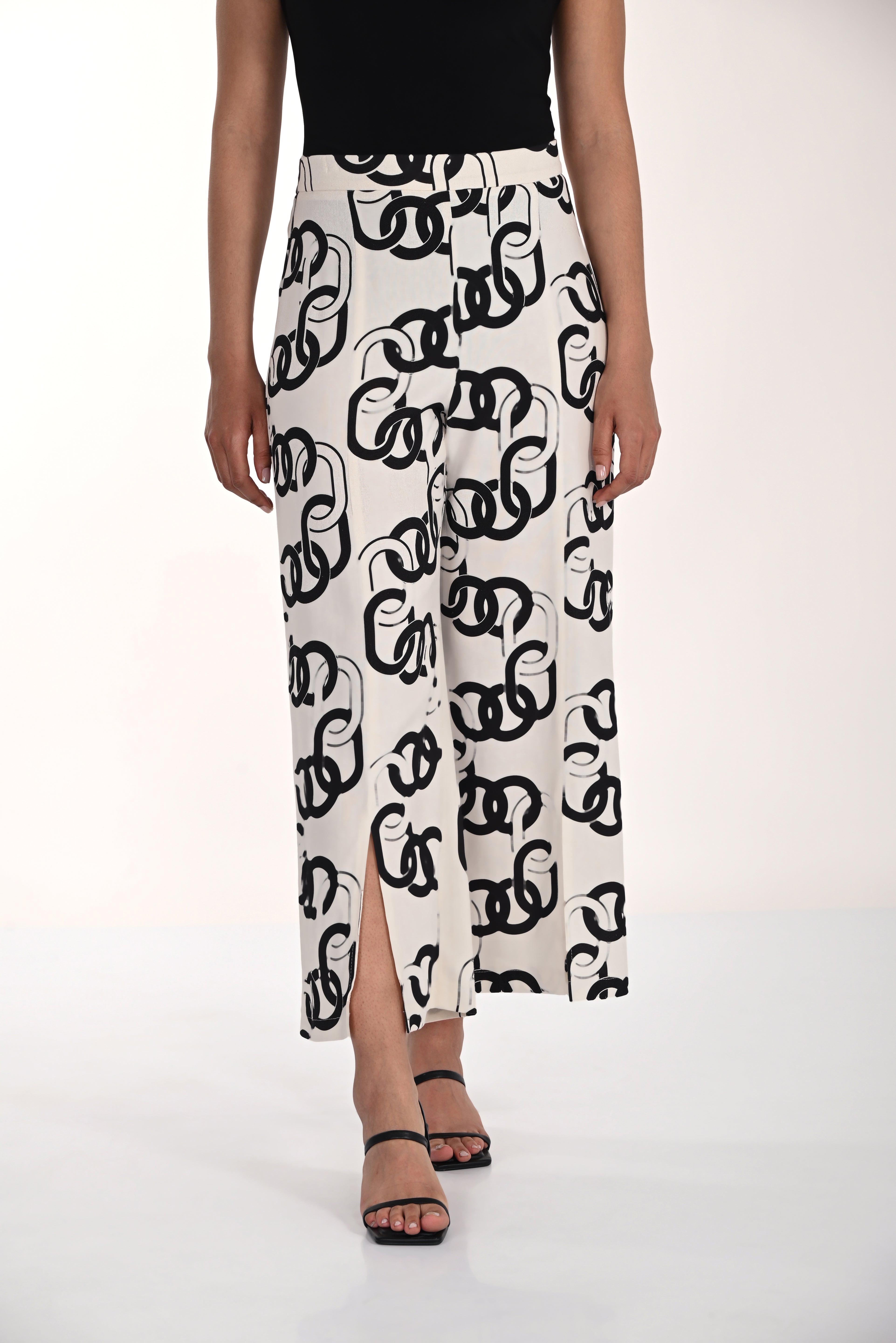 Model wearing a sleeveless fitted top paired with wide-leg chain print pants featuring a relaxed drape, front slit hem detail, and a flowing rayon-linen blend silhouette.