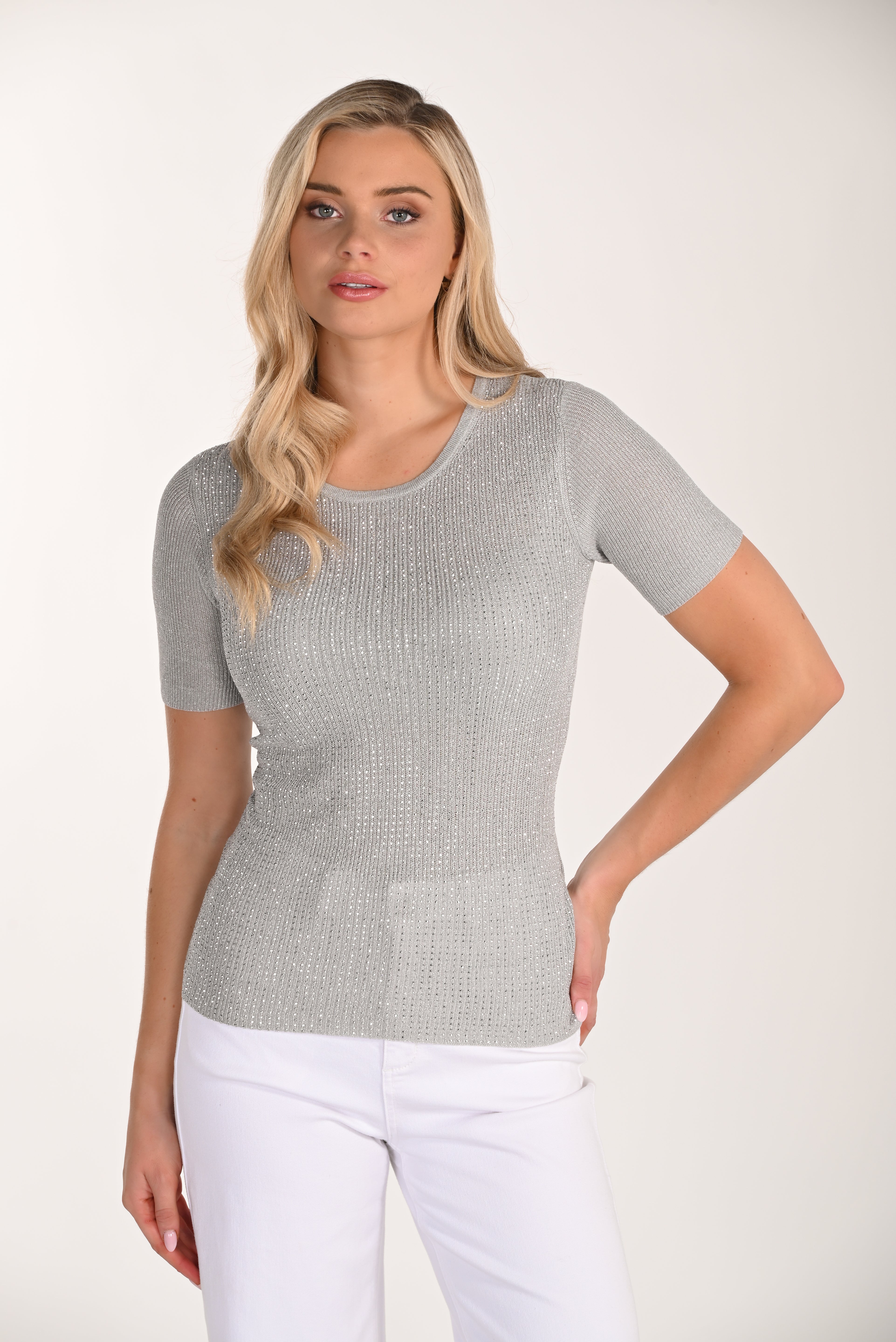 Front view of a women’s silver shimmer ribbed knit short sleeve top with a fitted silhouette and crew neckline paired with white pants.