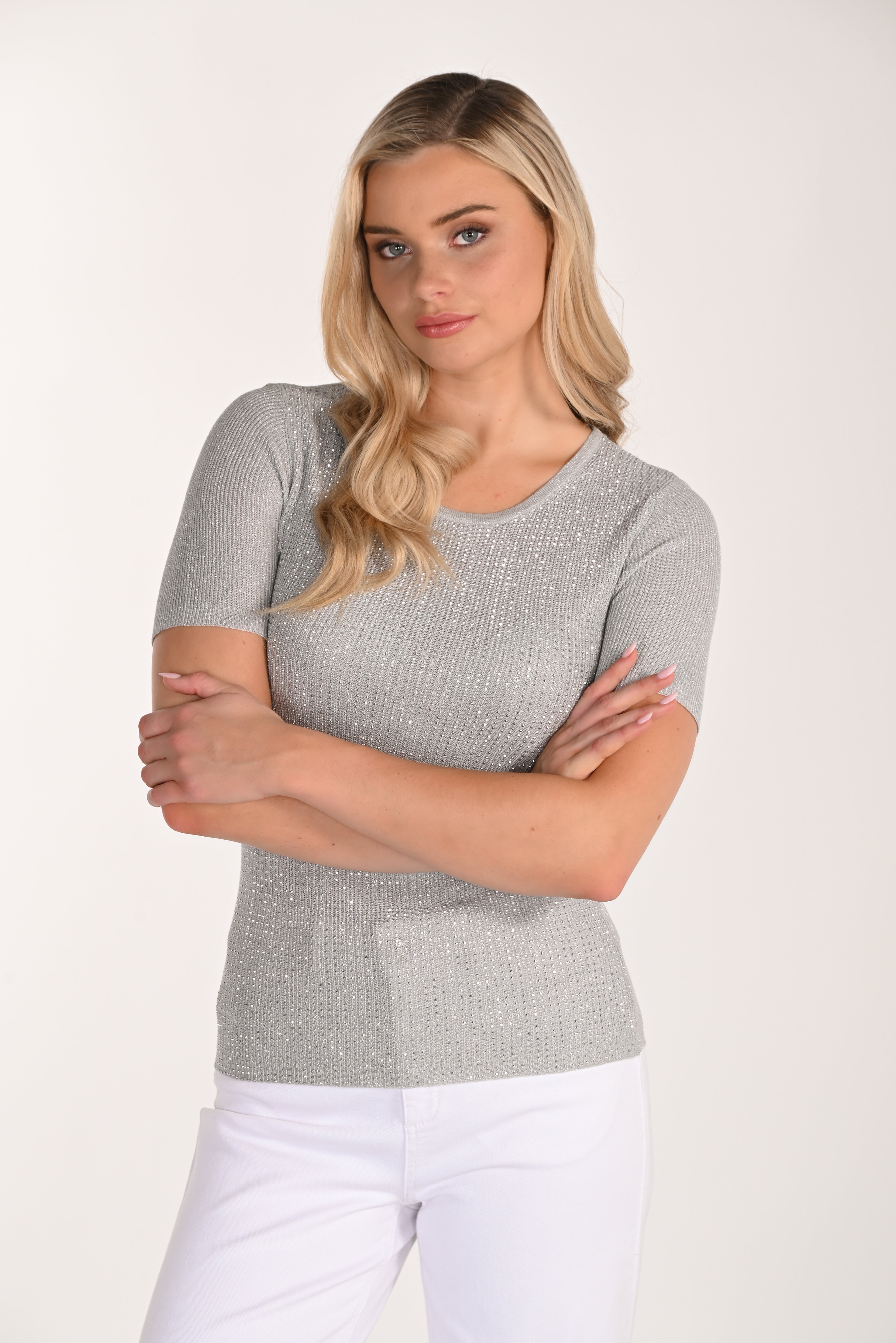 Front view of a women’s silver shimmer ribbed knit short sleeve top with a fitted silhouette and crew neckline paired with white pants.