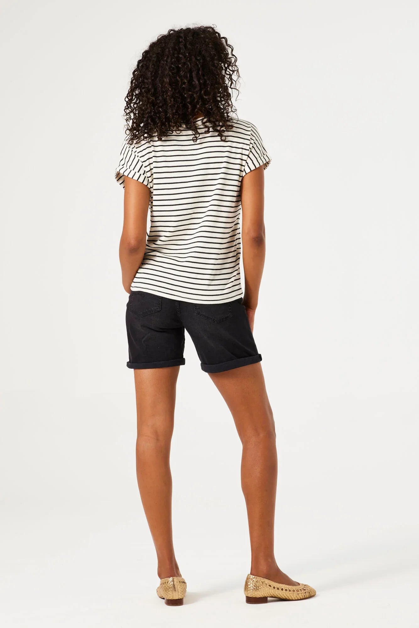 Woman wearing mid-length denim Bermuda shorts with rolled hems, shown from the back with a relaxed fit.