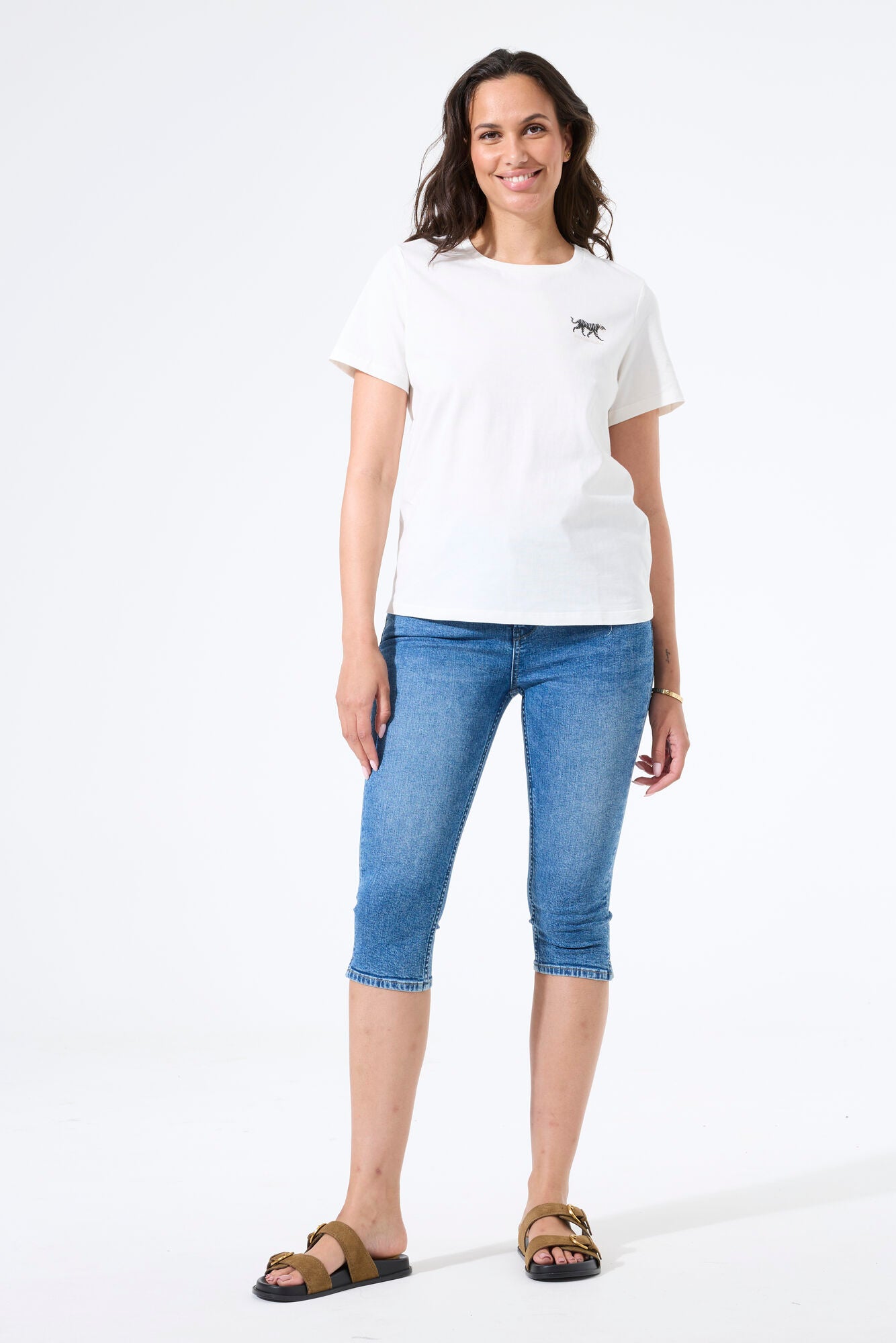Woman wearing a fitted capri-length denim pant paired with a short-sleeve t-shirt and slide sandals, shown from the front.