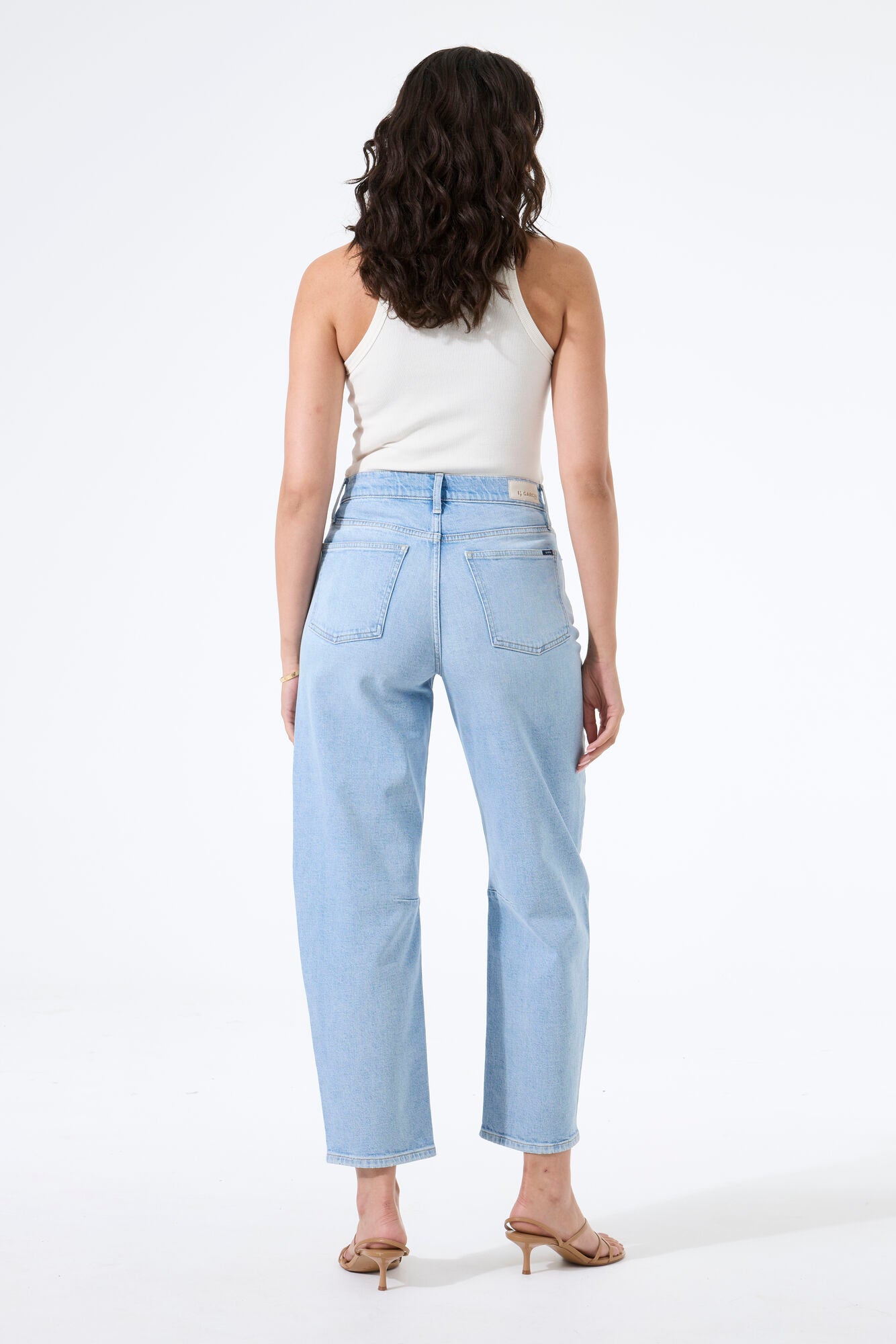 Model wearing light wash barrel-leg denim jeans with a fitted sleeveless top and heeled sandals, creating a casual, modern silhouette.