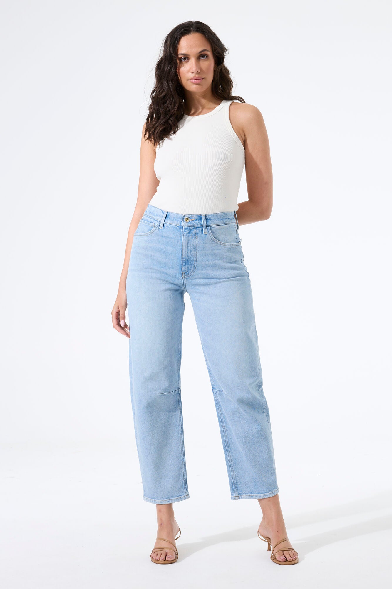 Model wearing barrel-leg denim jeans with a fitted sleeveless top and heeled sandals, creating a casual, modern silhouette.