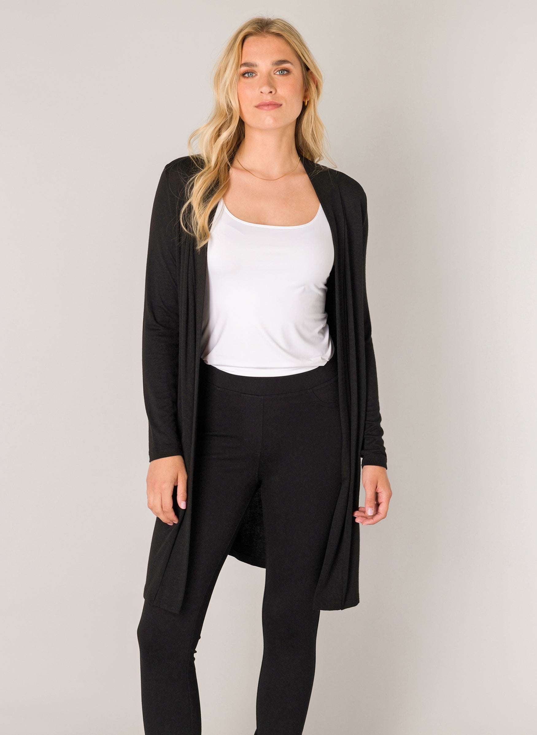 Women's black longline cardigan with an open-front design and long sleeves. Shown from the front, the cardigan is layered over a white tank top and black leggings, highlighting its soft drape and comfortable fit.