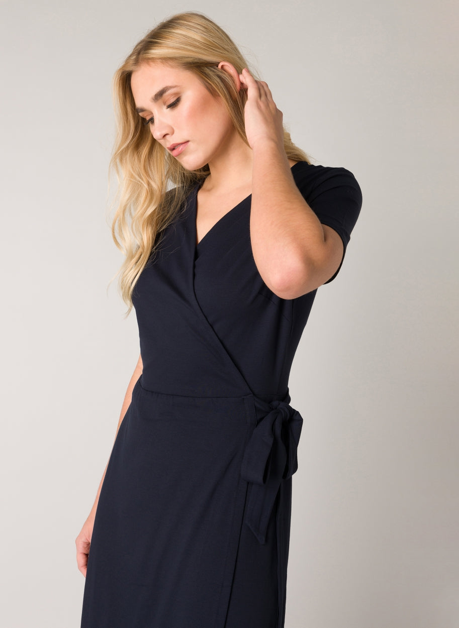 Close-up of a women's black wrap midi dress highlighting the V-neckline, wrap-front bodice, and side tie detail. The soft viscose-blend fabric provides a smooth finish with comfortable stretch.