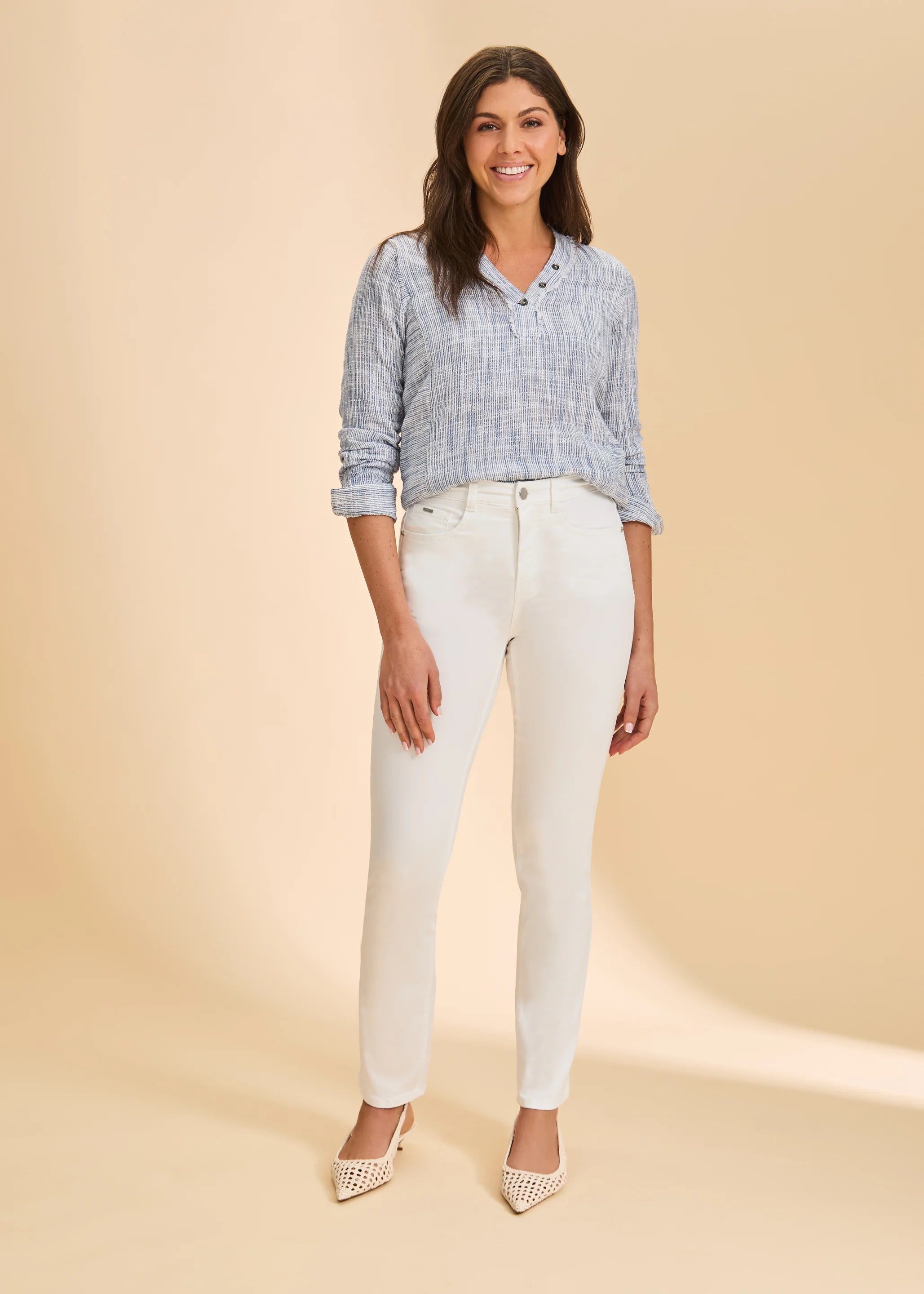 Full-length view of a woman wearing slim straight-leg pants in a light neutral tone, styled with a relaxed long sleeve top and pointed low heels for a polished everyday look.