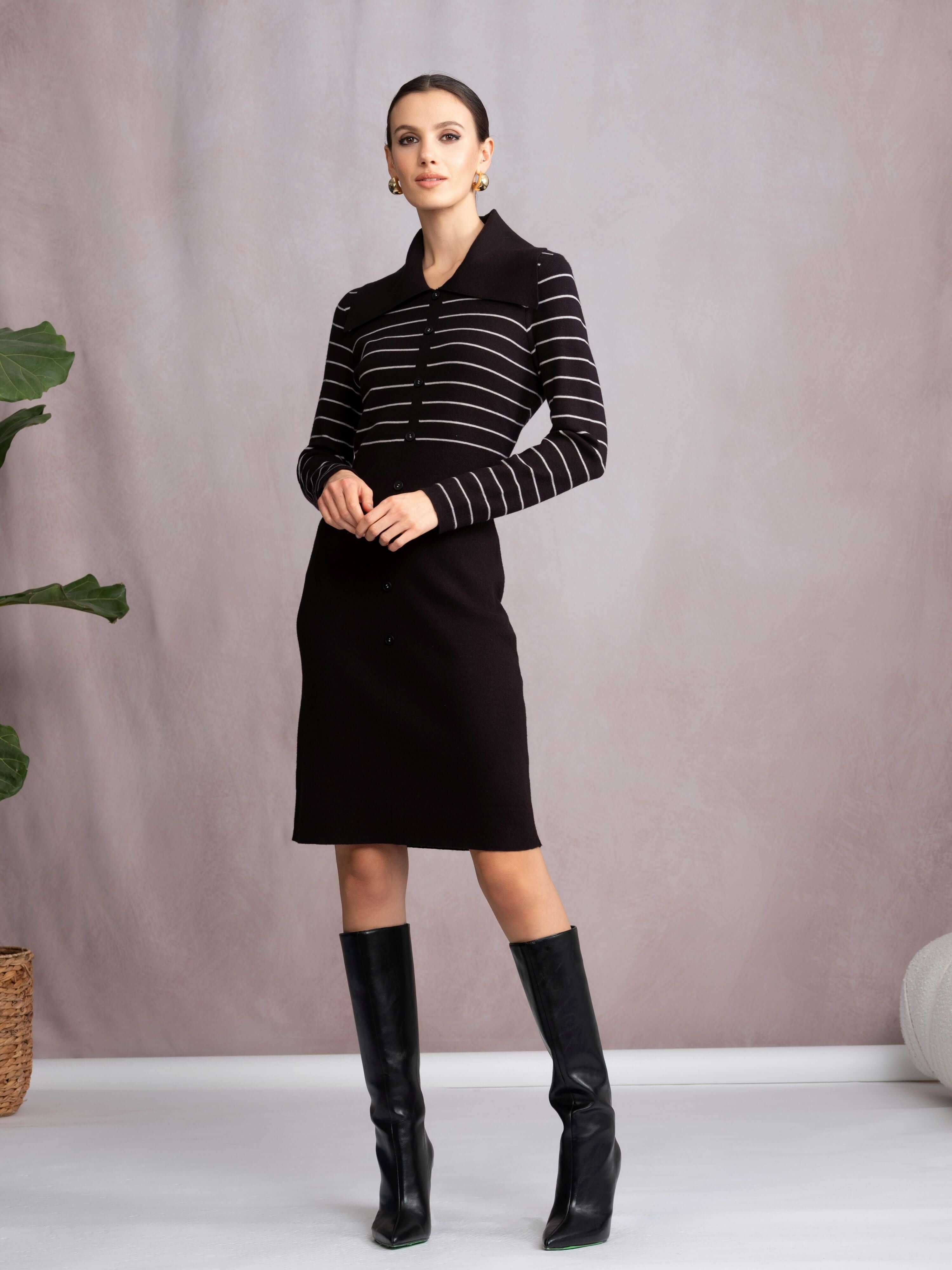 Woman wearing a black and white striped sweater dress with black boots against a plain background