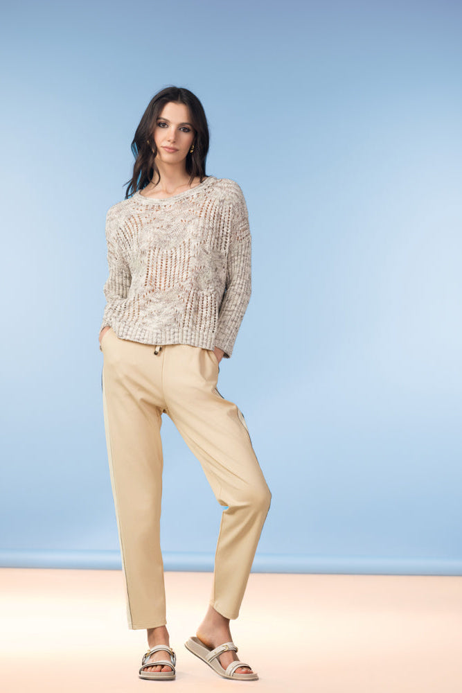 Woman wearing a beige sweater and pants against a light blue background