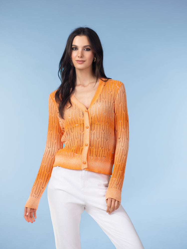 Model wearing a bright orange open-knit V-neck cardigan with button-front closure, styled with light trousers against a blue backdrop.