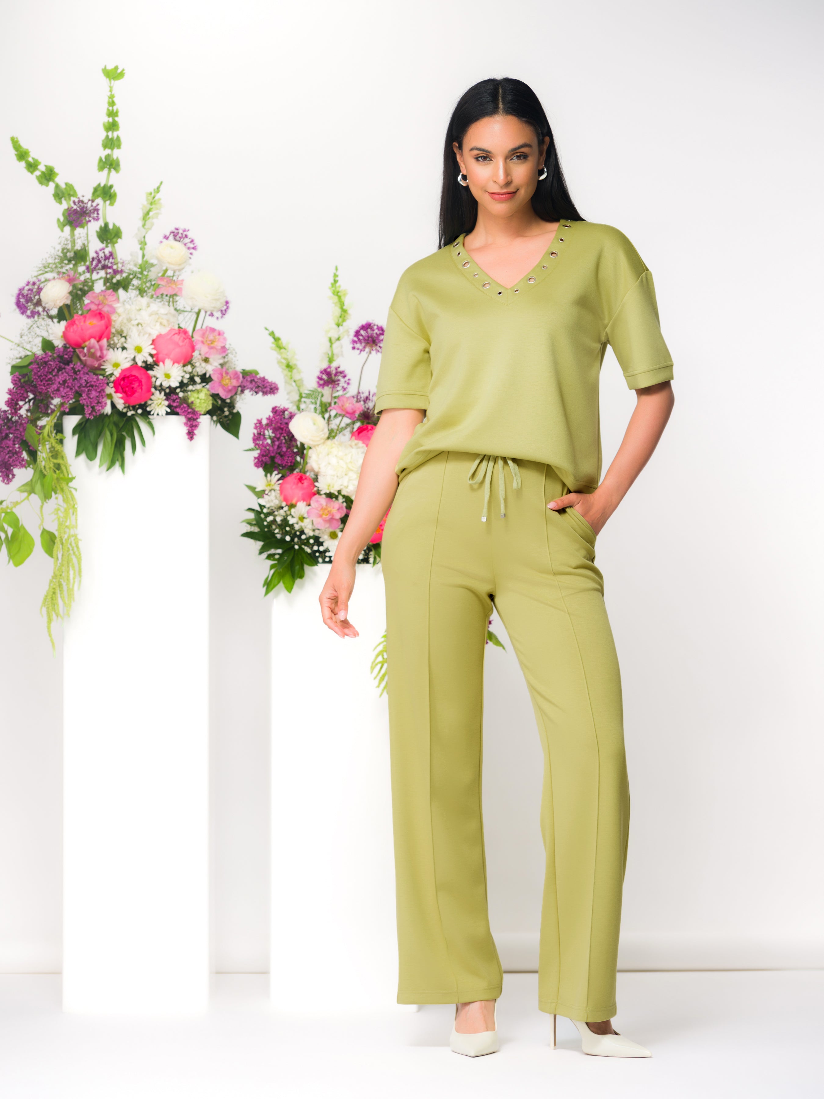Woman wearing a relaxed lime green V-neck top with short sleeves and matching wide-leg pants, styled indoors with floral arrangements.