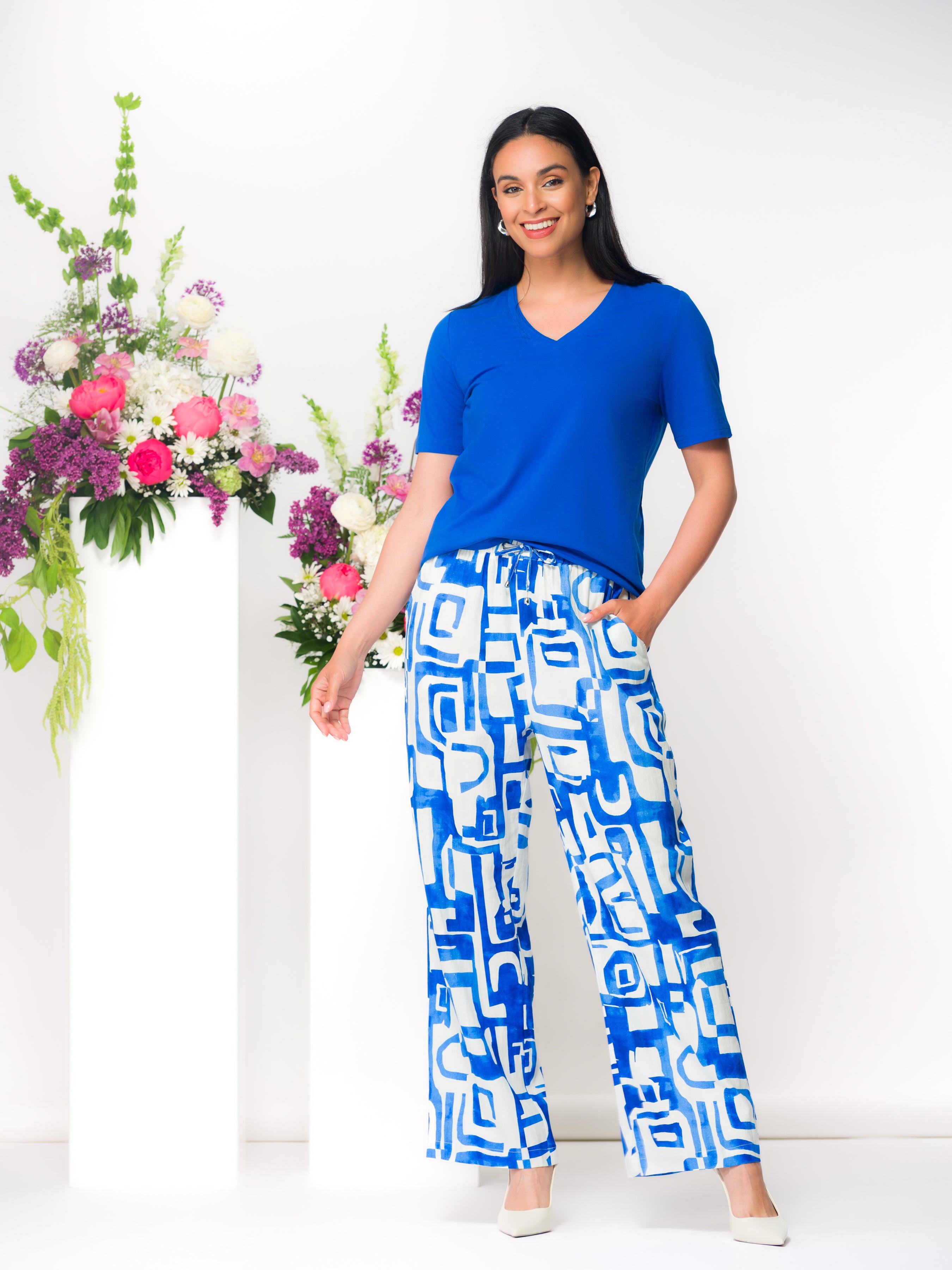 Woman wearing a blue short-sleeve V-neck cotton-blend tee with a relaxed fit, styled with blue and white pants for a polished everyday look.