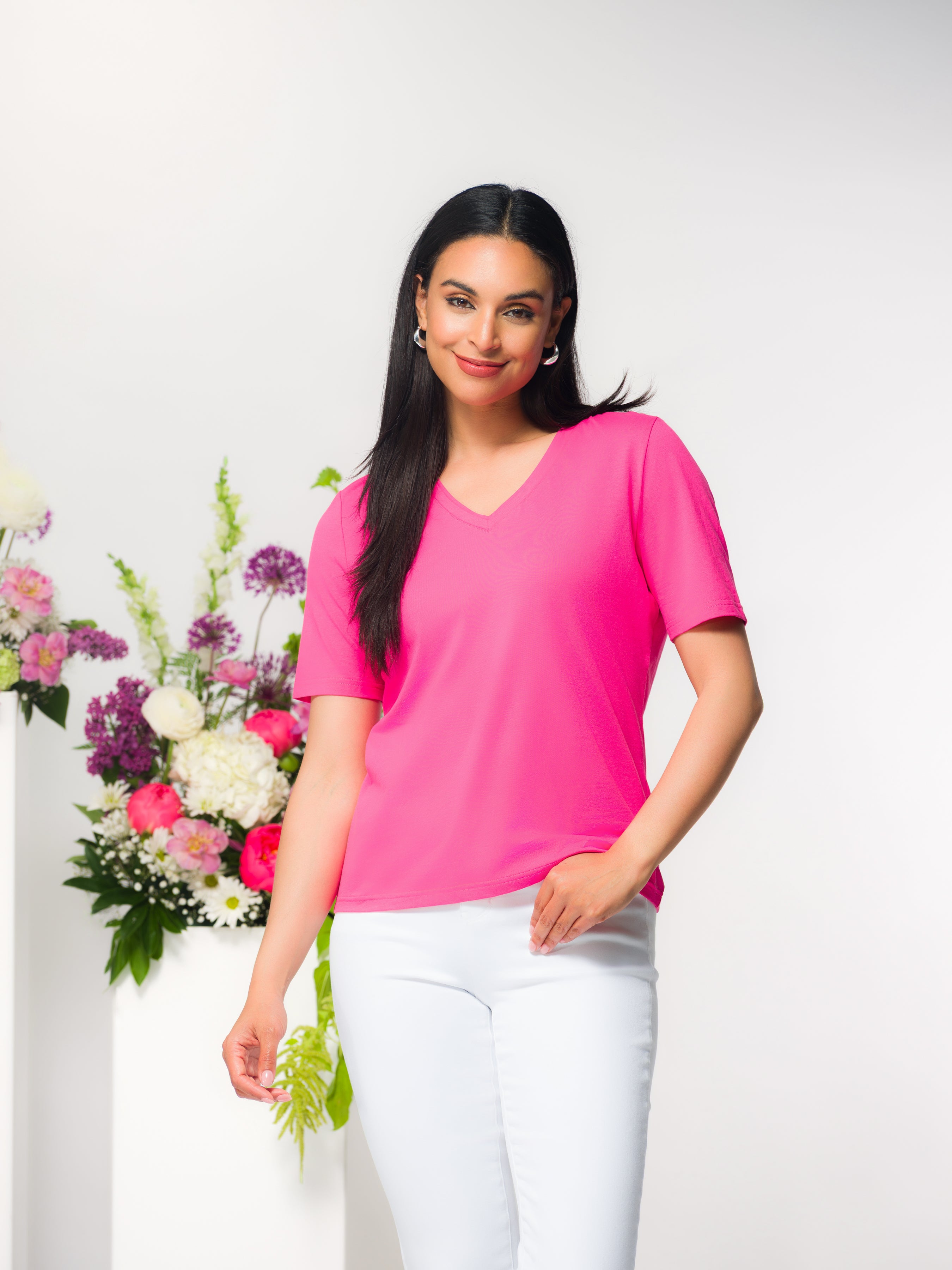 Woman wearing a pink short-sleeve V-neck cotton-blend tee with a relaxed fit, styled with a slim-fit white pants for a polished everyday look.
