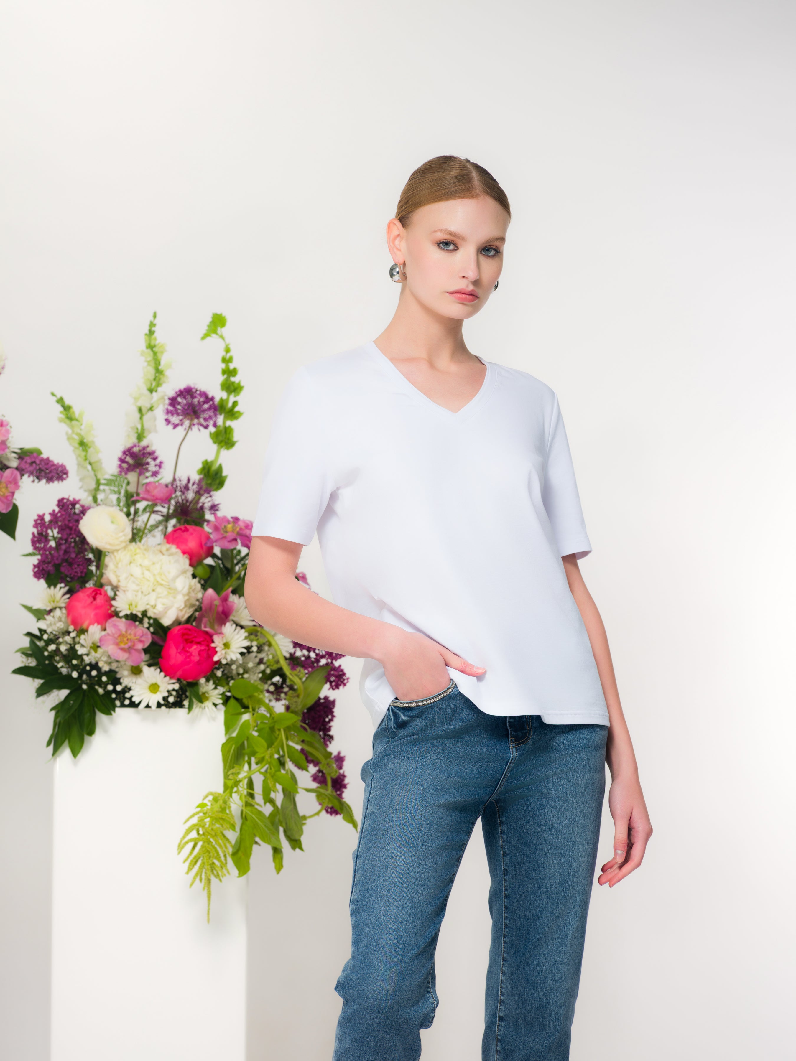 Woman wearing a white short-sleeve V-neck cotton-blend tee with a relaxed fit, styled with denim jeans for a polished everyday look.