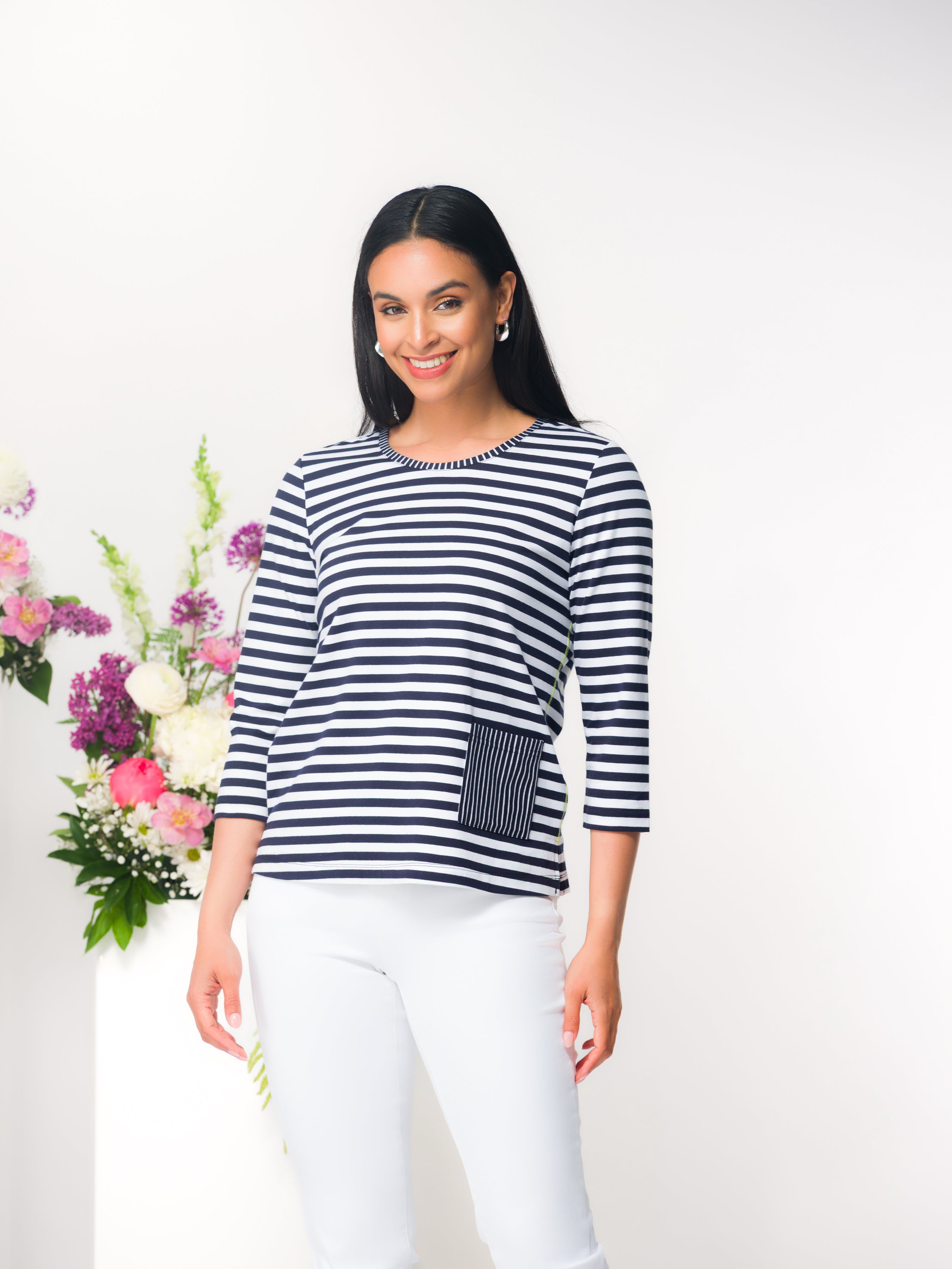Women’s relaxed-fit blue and white striped knit top with three-quarter length sleeves, a round neckline, and a front patch pocket detail, styled with fitted pants in a studio setting.