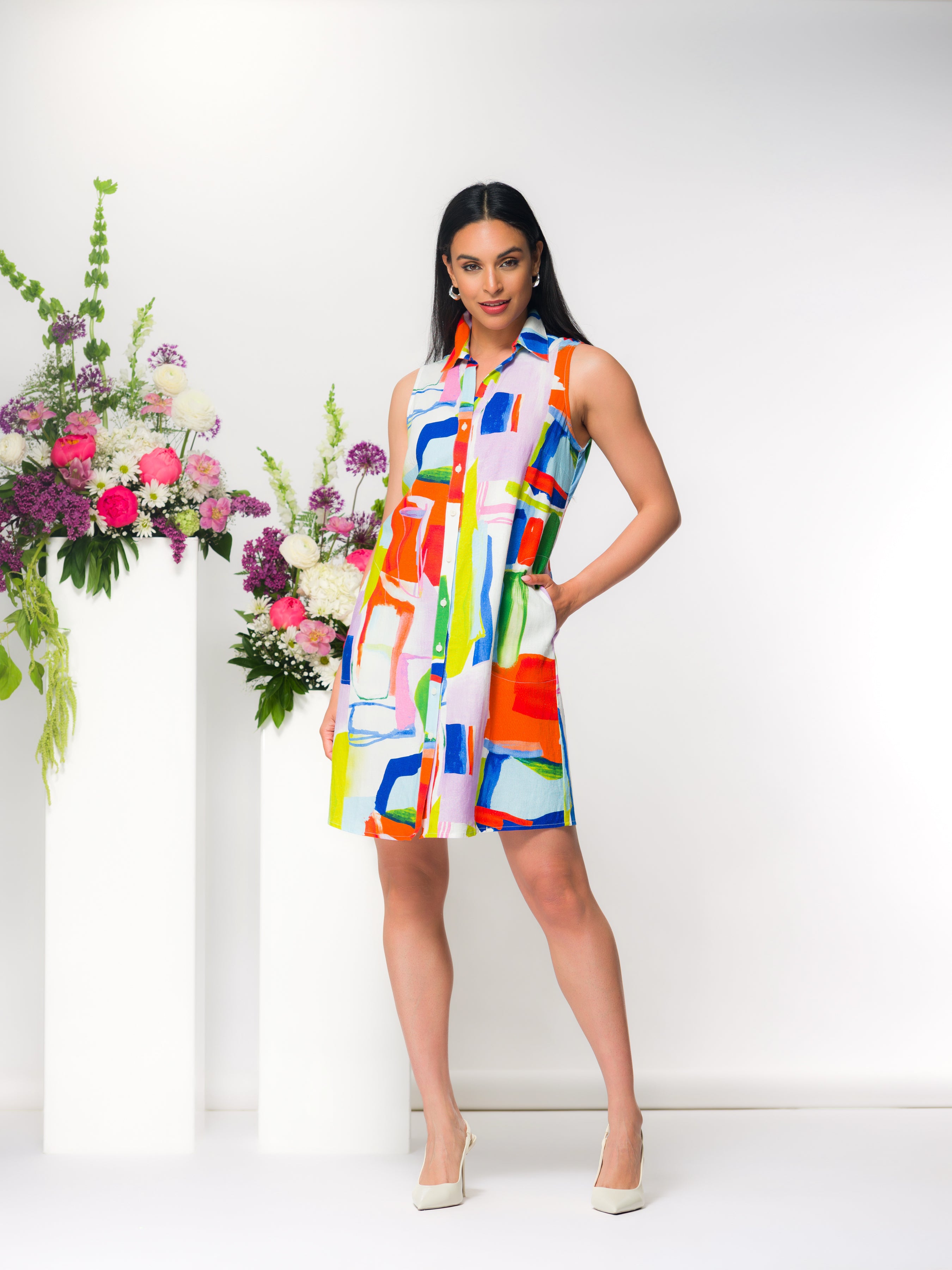 Women wearing a sleeveless button-front shirt dress with a relaxed fit and above-the-knee length, styled with heels in a studio setting.