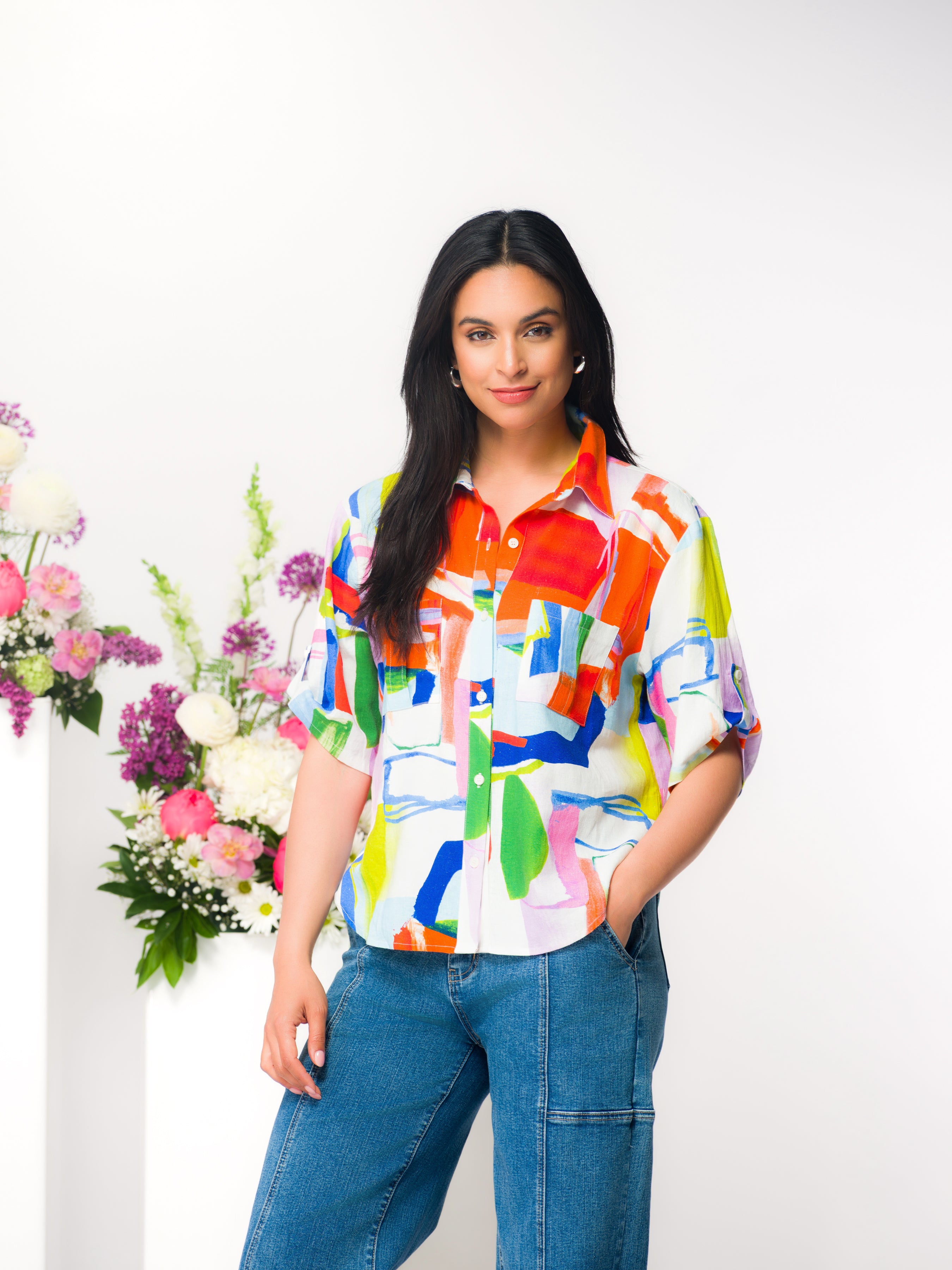 Women’s relaxed button-up shirt with short sleeves and a soft drape, styled with jeans, photographed on a model in a studio setting.